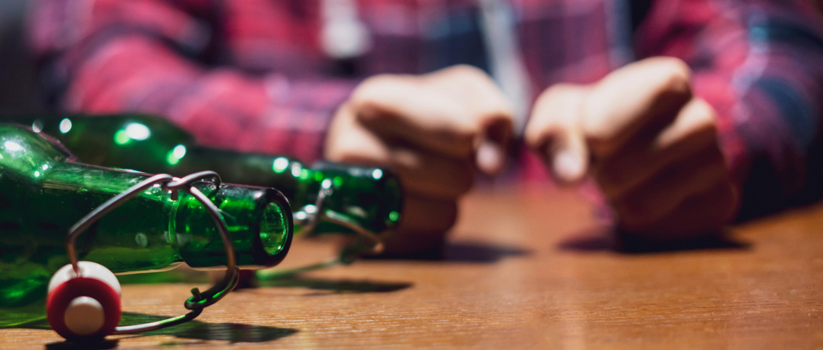 Zwei leere Bierflaschen liegen auf einem Tisch. Dahinter ballt ein Mensch angespannt zwei Fäuste.