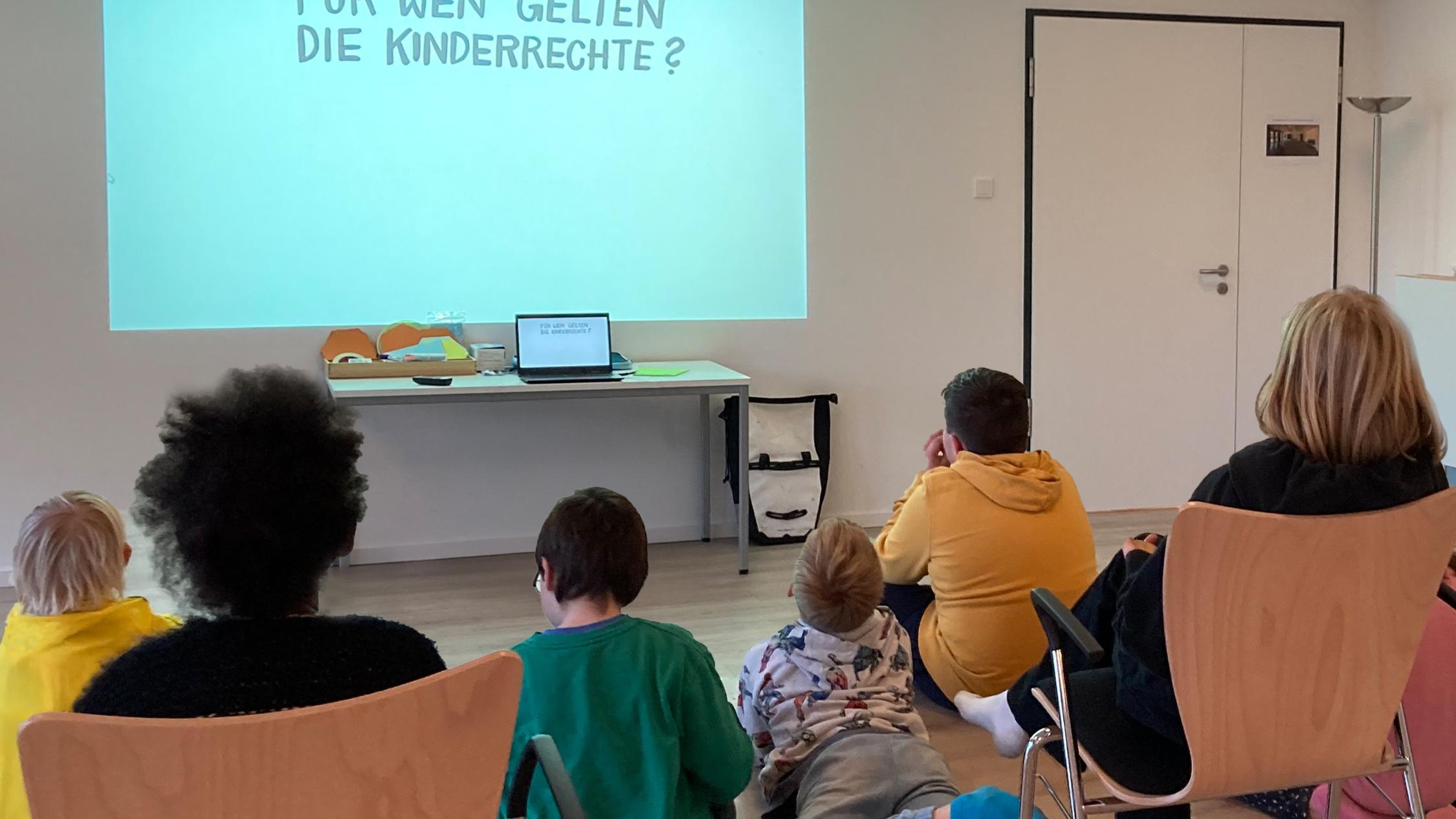 Kinder sitzen interssiert vor einer Präsentation in einem geschützen Raum und lernen ihre Rechte kennen