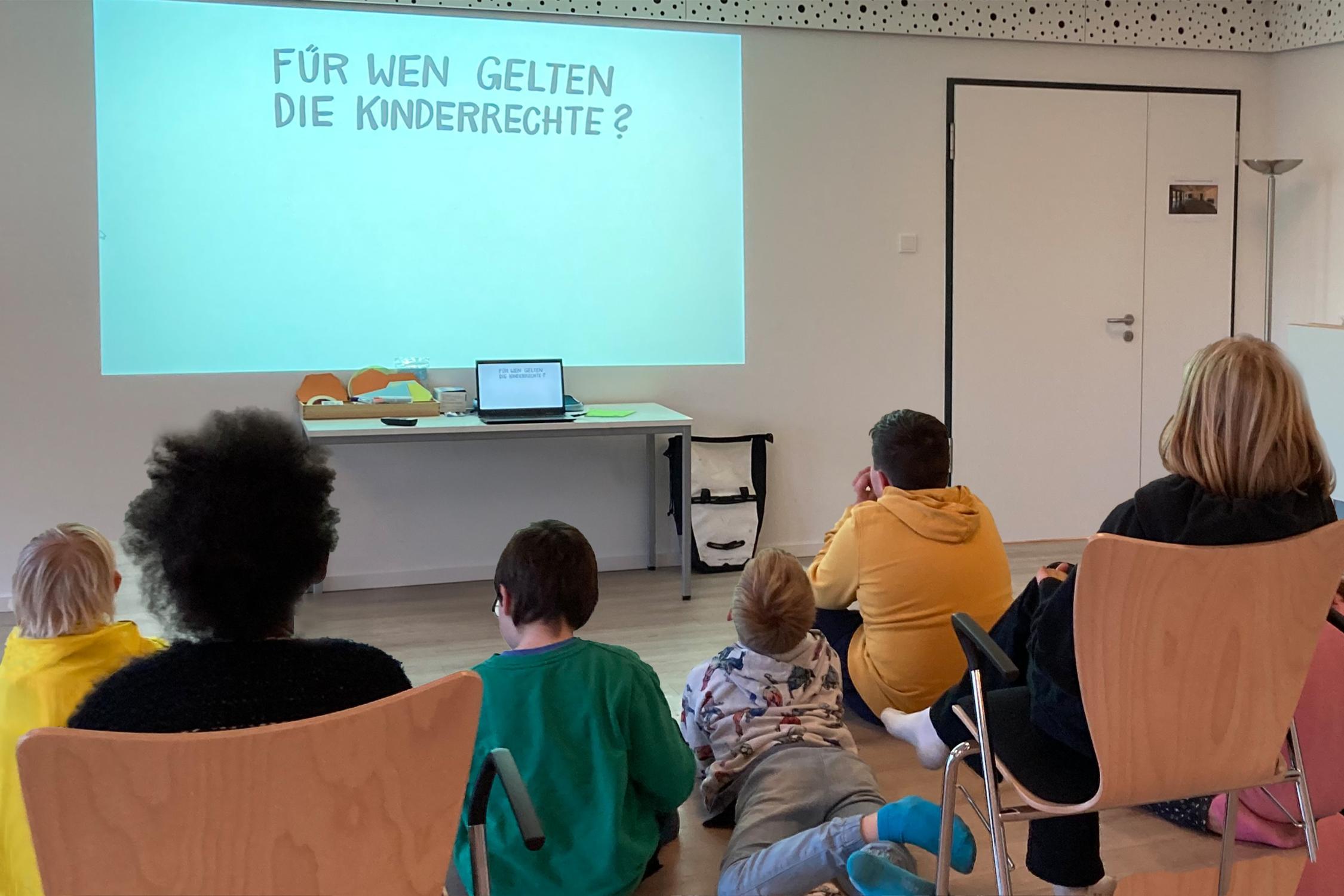 Kinder sitzen interssiert vor einer Präsentation in einem geschützen Raum und lernen ihre Rechte kennen