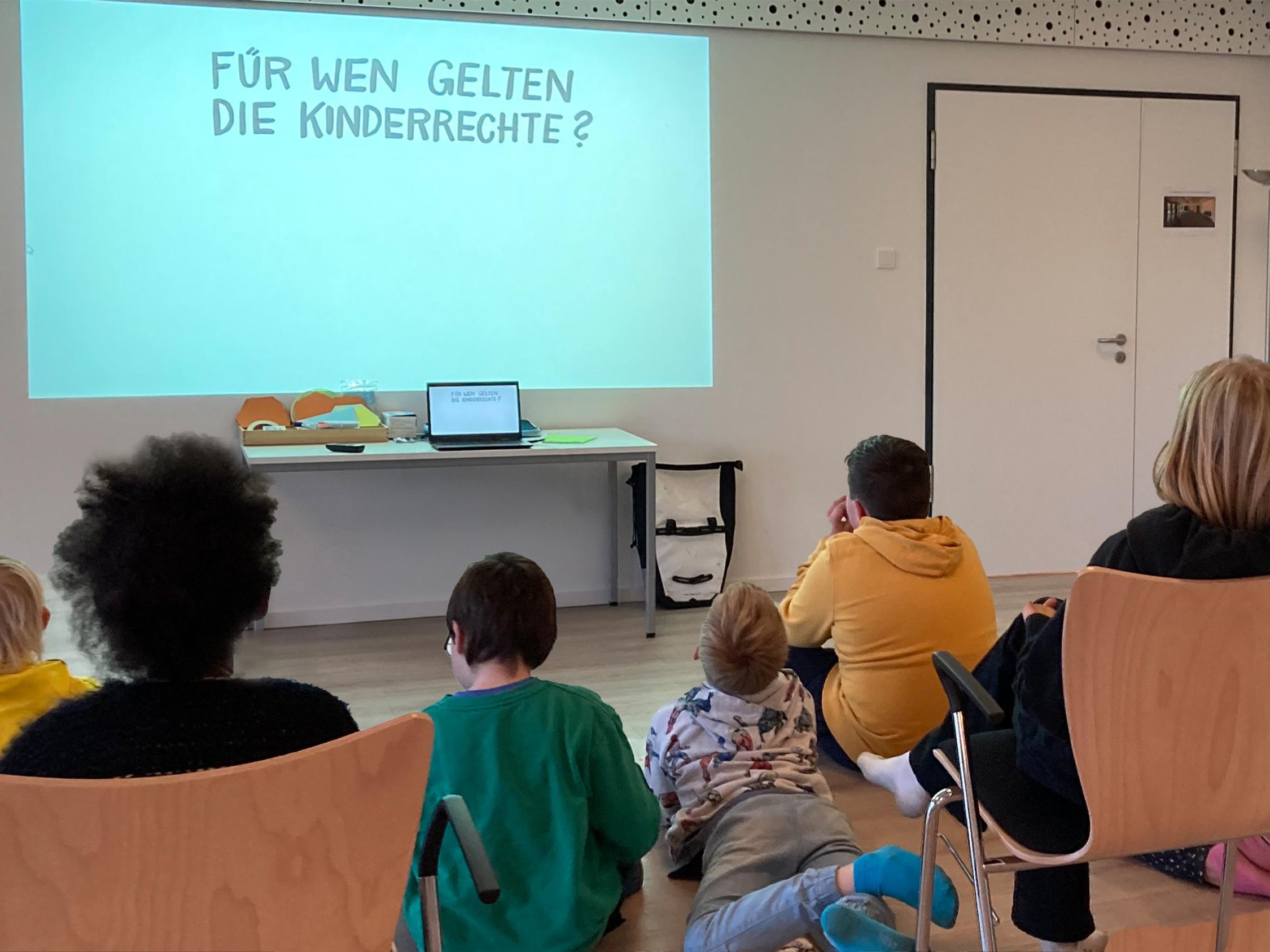 Kinder sitzen interssiert vor einer Präsentation in einem geschützen Raum und lernen ihre Rechte kennen