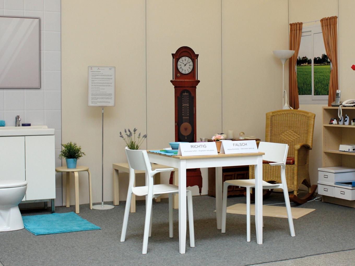 Gegenstände und Möbel des täglichen Lebens stehen mit Erläuterungen aufgebaut in der Demenzmusterwohnung