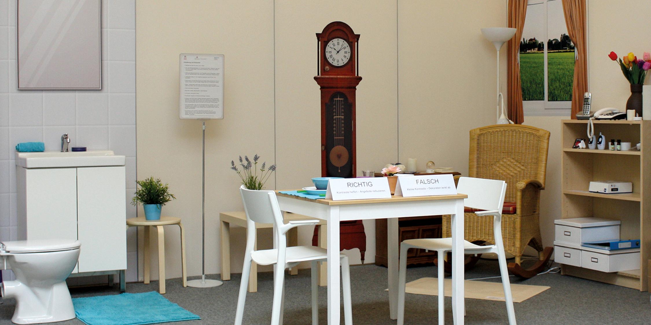 Gegenstände und Möbel des täglichen Lebens stehen mit Erläuterungen aufgebaut in der Demenzmusterwohnung
