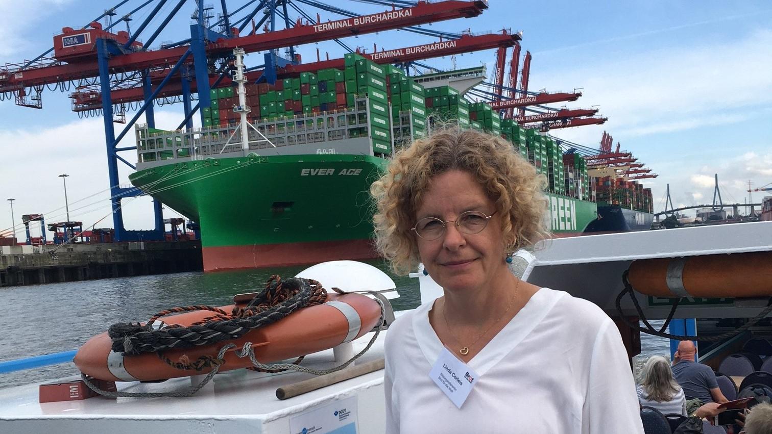 Eine Frau steht auf einer Elb-Barkasse. Im Hintergrund befindet sich ein beladenes Containerschiff