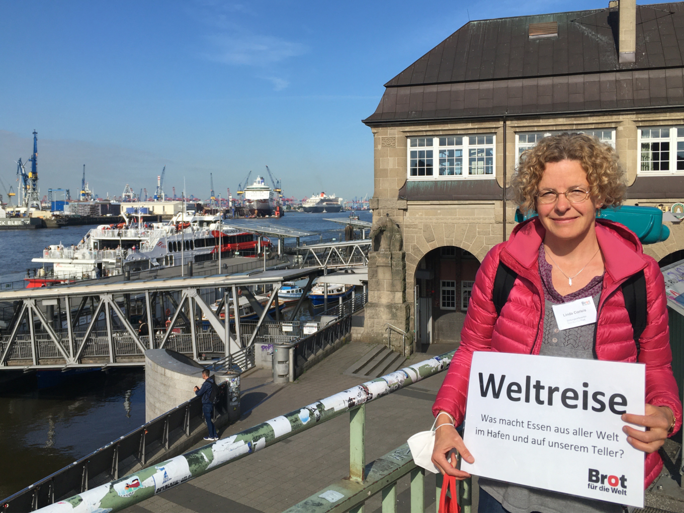 Eine Frau steht vor den Landungbrücken in Hamburg. Barkassenfahrt zum Thema: Was macht Essen aus aller Welt im Hafen und auf unserem Teller?