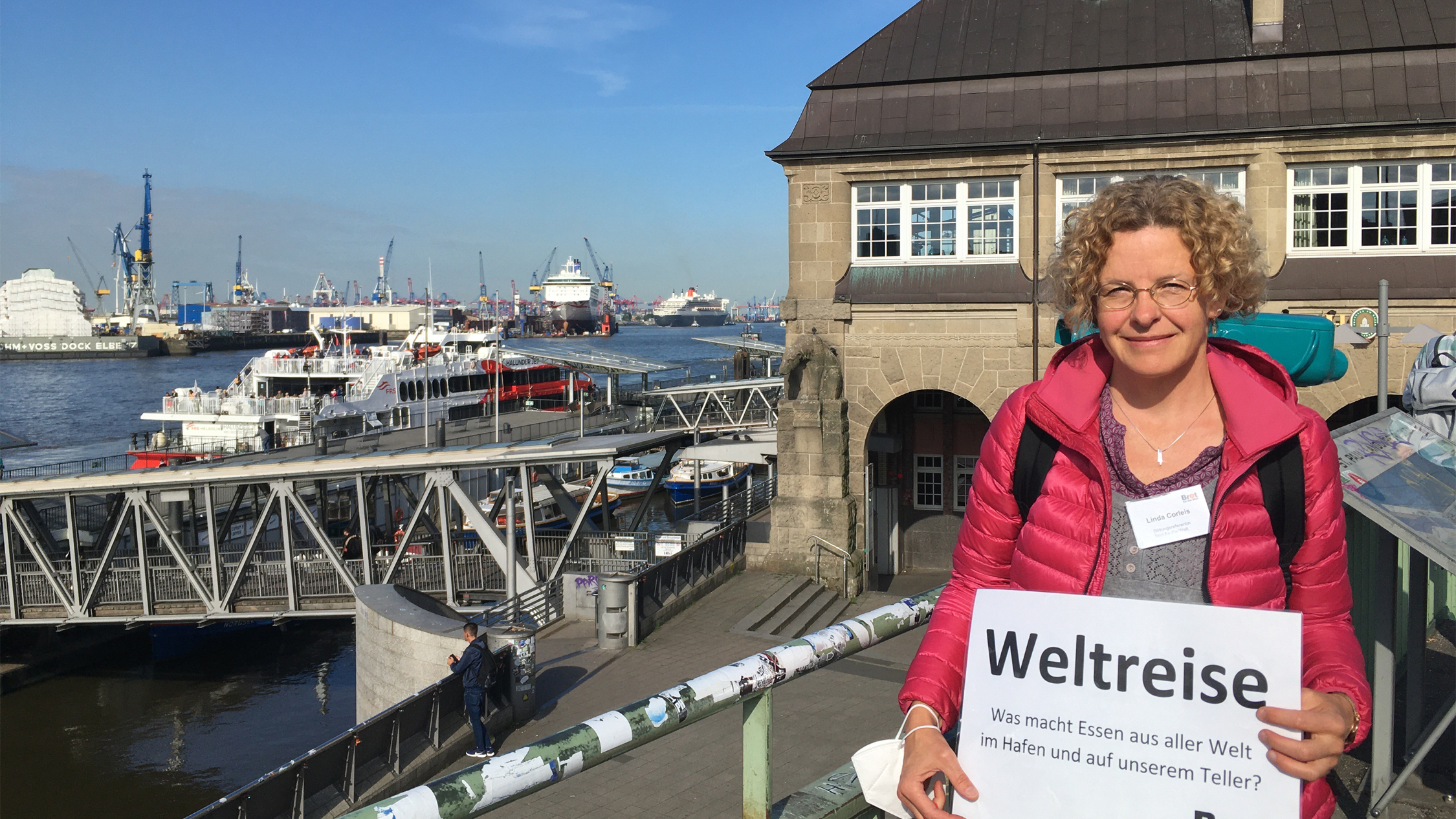 Eine Frau steht vor den Landungbrücken in Hamburg. Barkassenfahrt zum Thema: Was macht Essen aus aller Welt im Hafen und auf unserem Teller?