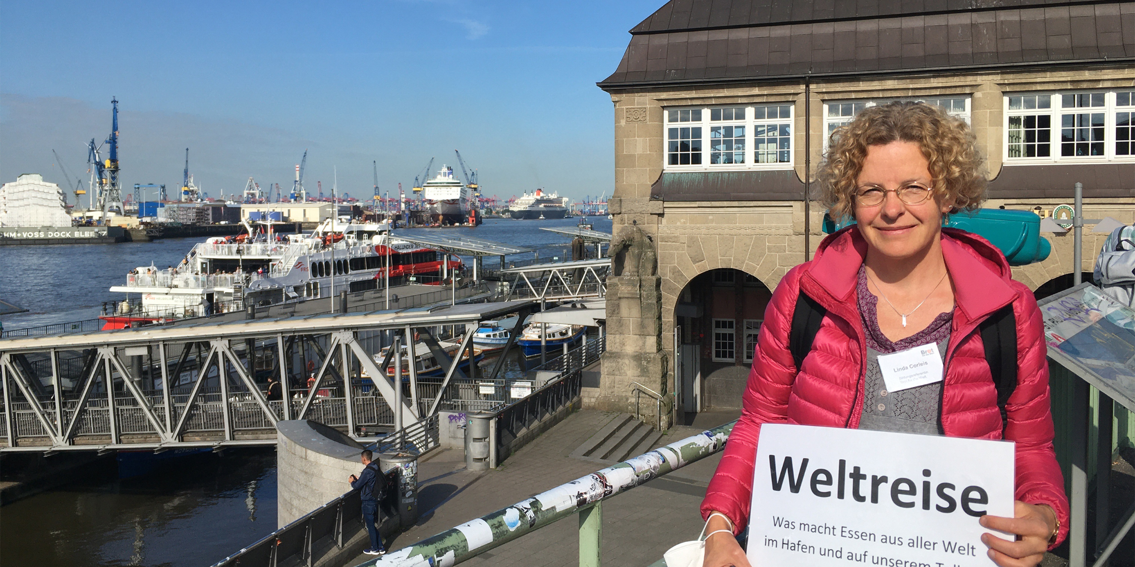 Eine Frau steht vor den Landungbrücken in Hamburg. Barkassenfahrt zum Thema: Was macht Essen aus aller Welt im Hafen und auf unserem Teller?