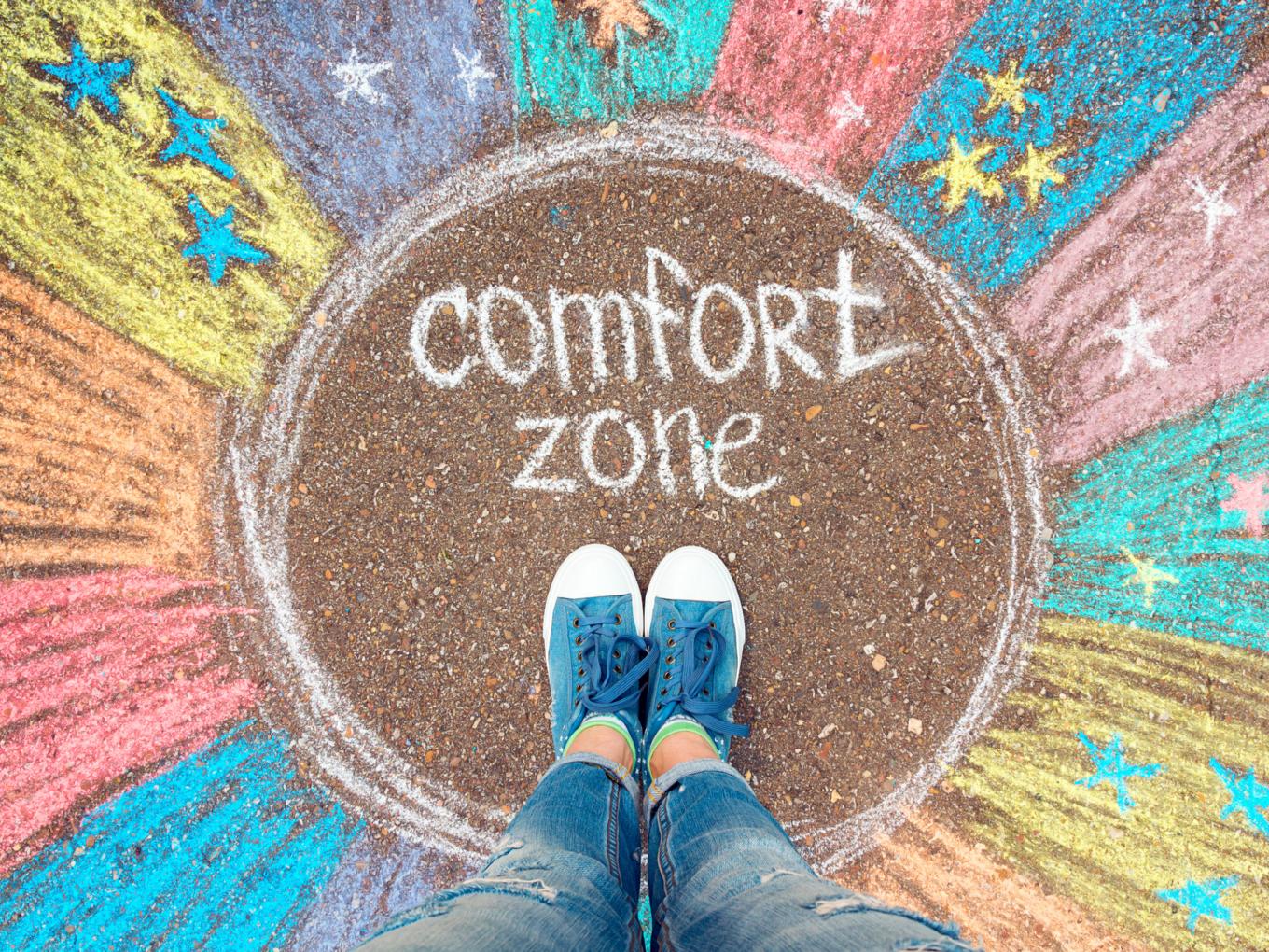 EIne Person steht in einem bunten, mit Kreide gemalten Kreis mit dem Text: comfort zone