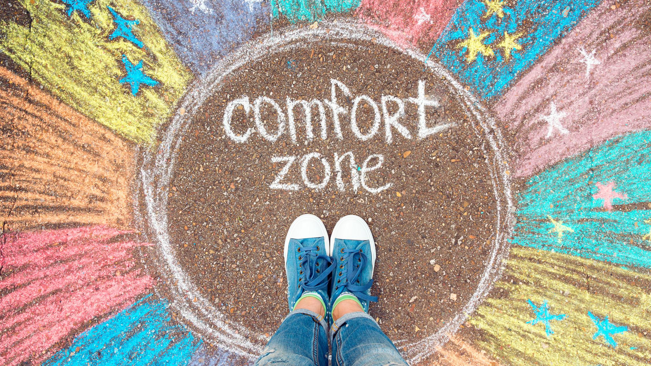 EIne Person steht in einem bunten, mit Kreide gemalten Kreis mit dem Text: comfort zone