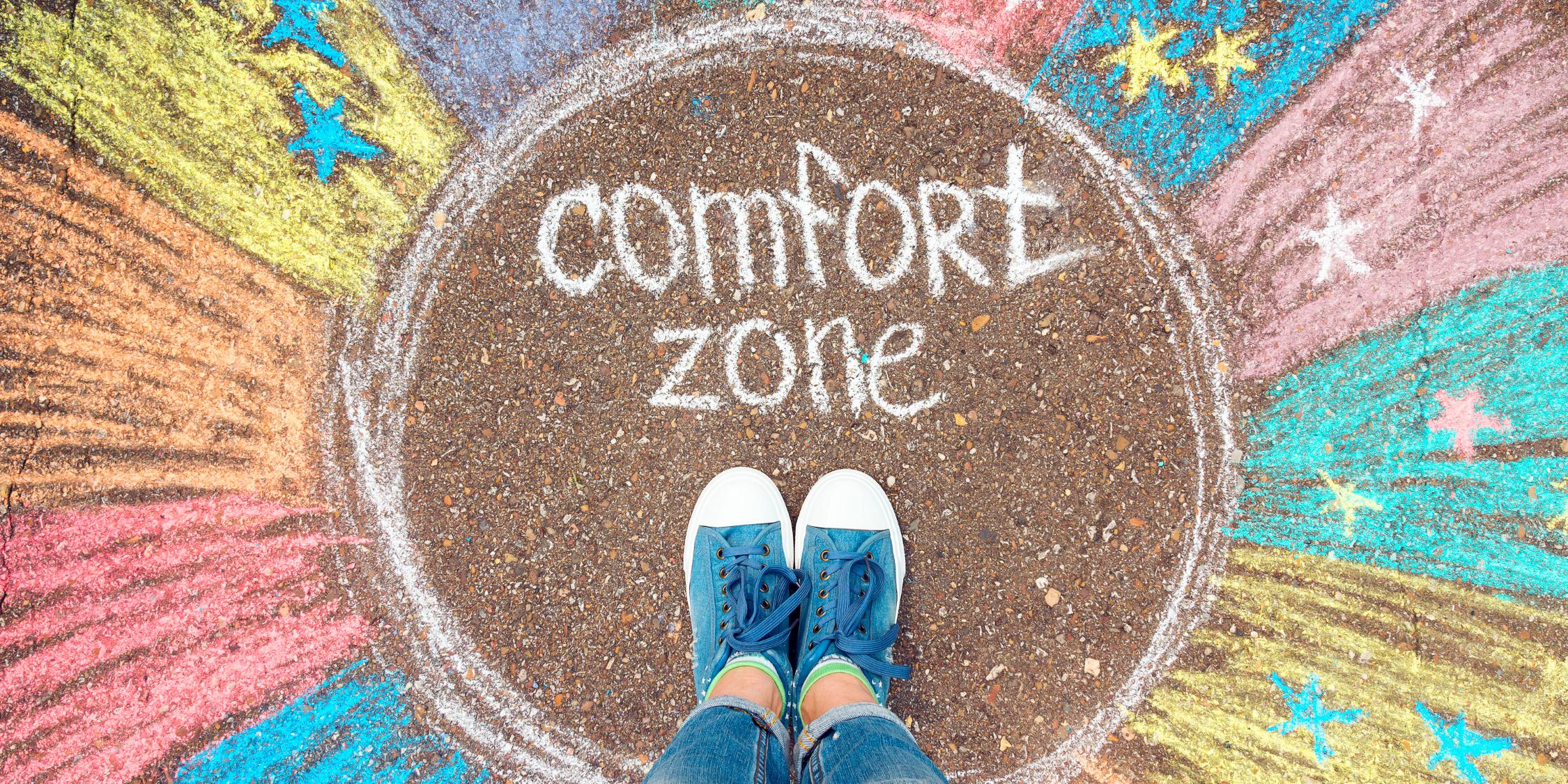 EIne Person steht in einem bunten, mit Kreide gemalten Kreis mit dem Text: comfort zone