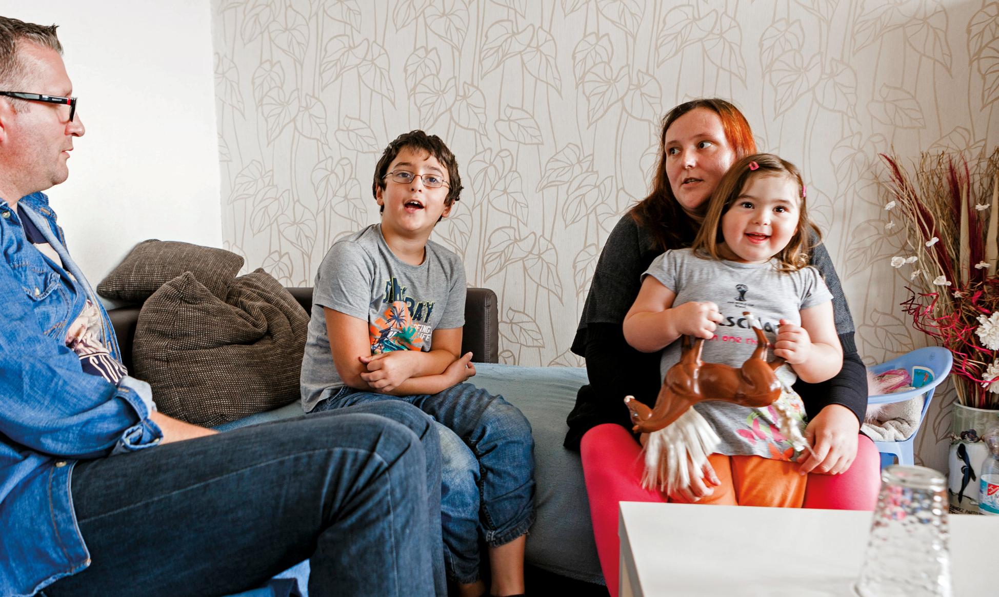 Vater, Mutter, Sohn und Tochter sitzen in einem Wohnzimmer auf einem Sofa und unterhalten sich