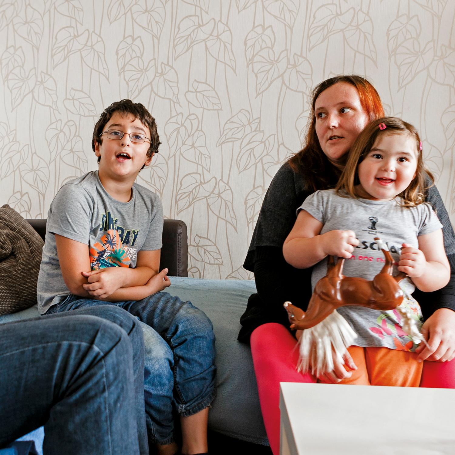 Vater, Mutter, Sohn und Tochter sitzen in einem Wohnzimmer auf einem Sofa und unterhalten sich