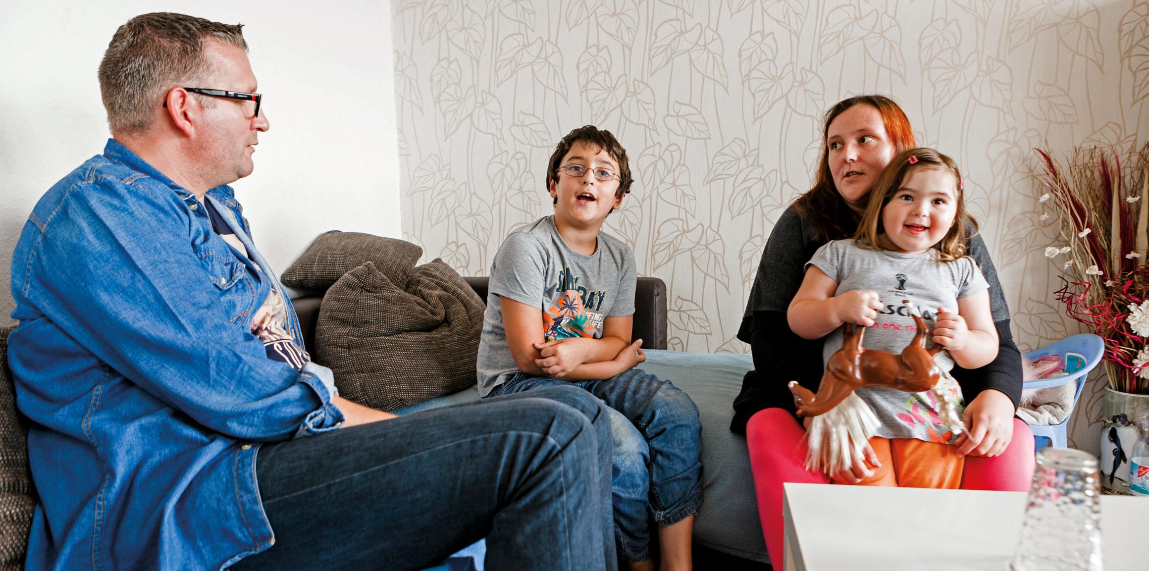Vater, Mutter, Sohn und Tochter sitzen in einem Wohnzimmer auf einem Sofa und unterhalten sich
