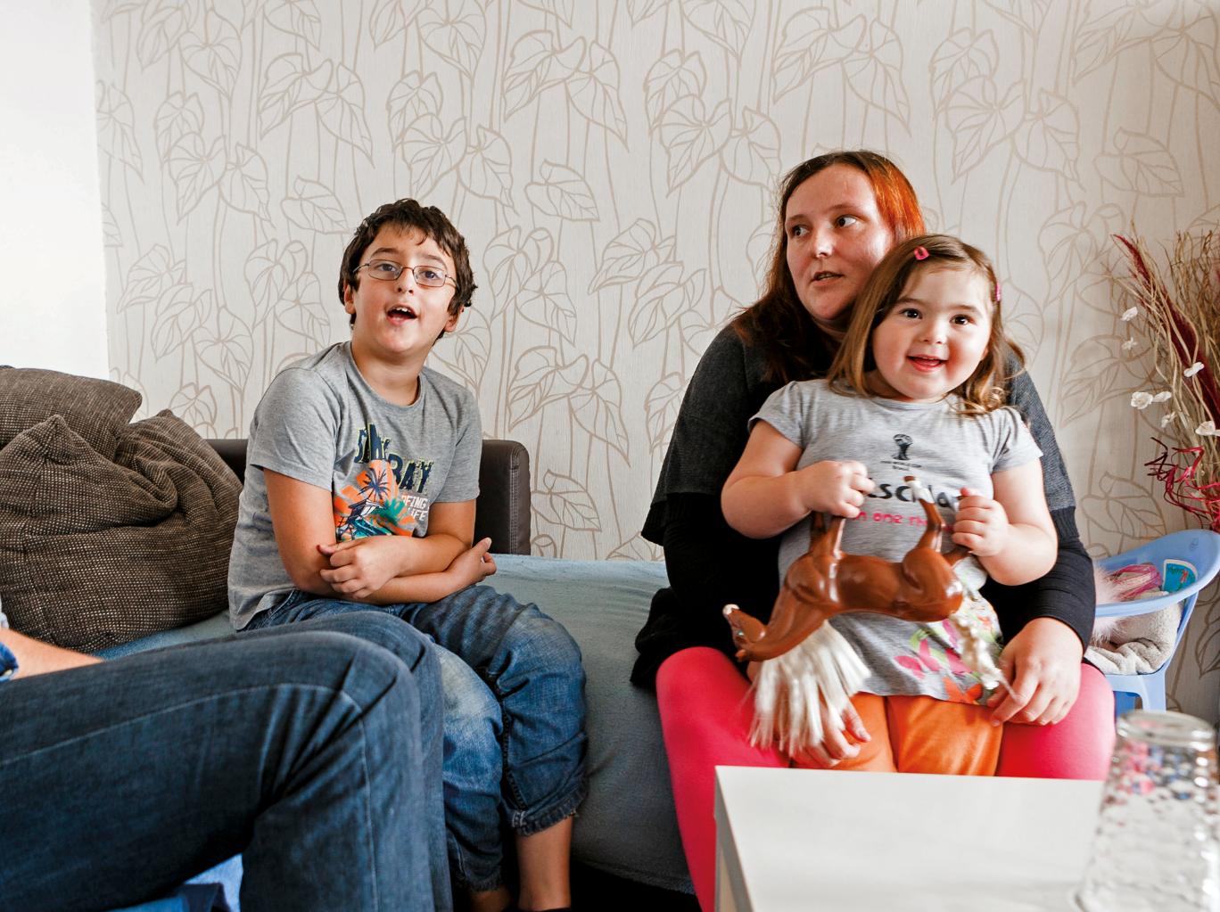 Vater, Mutter, Sohn und Tochter sitzen in einem Wohnzimmer auf einem Sofa und unterhalten sich