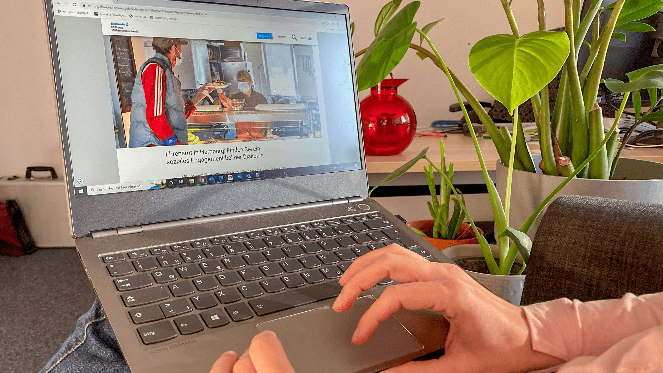 Eine Person balanciert einen Laptop auf dem Schoß und klickt sich durch die Website der Diakonie zur Ehrenamtsuche.