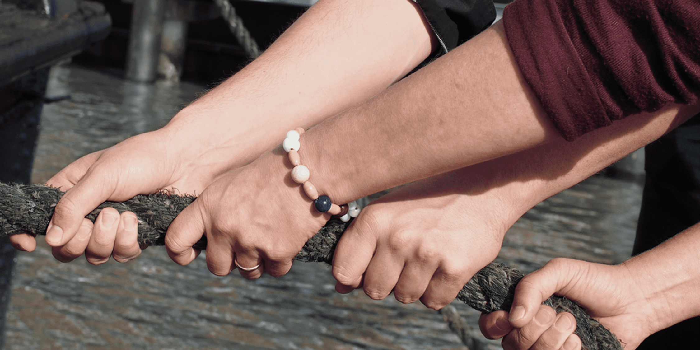 Vier Hände ziehen an einem Seil, eine Person trägt Ehering und Armband.