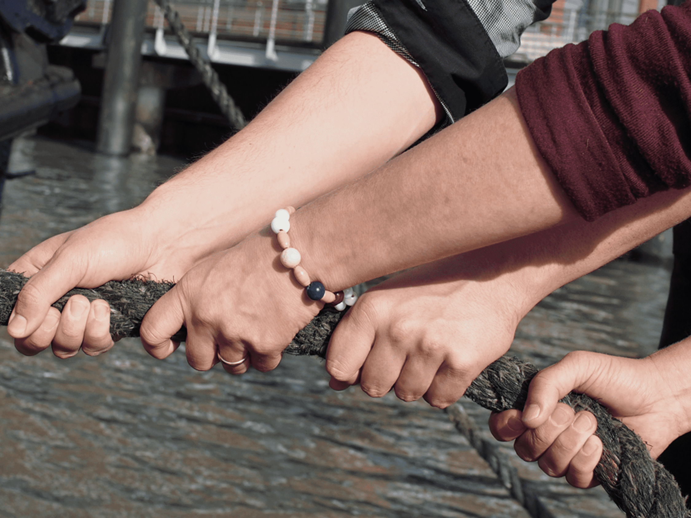 Vier Hände ziehen an einem Seil, eine Person trägt Ehering und Armband.