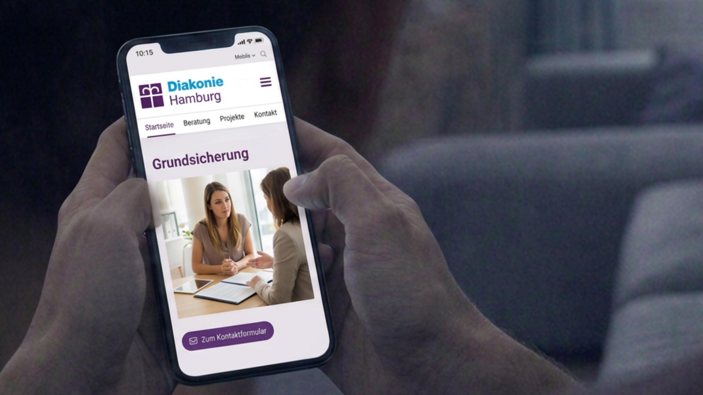 Man schaut einem Mann über die Schulter auf sein Smartphone, auf dem die Website der Diakonie Hamburg geöffnet ist.