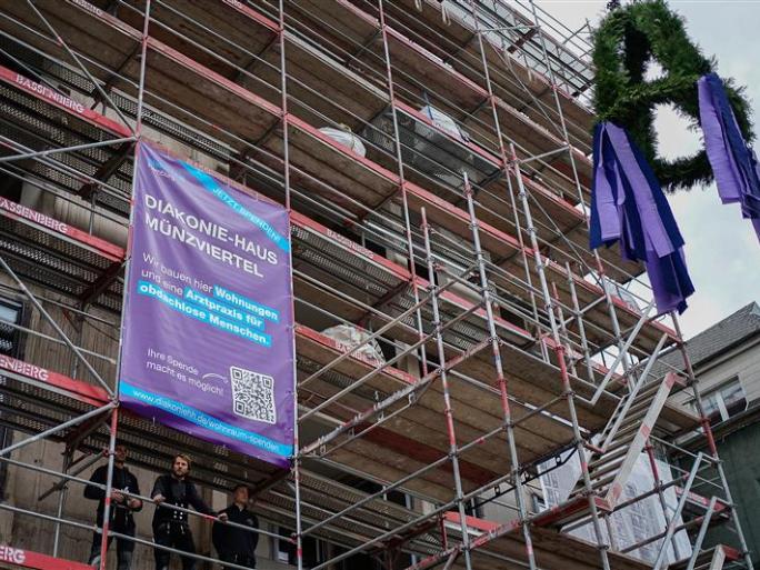 Ein Baugerüst an einem entstehenden Haus mit einem lila Banner und einem Kranz.