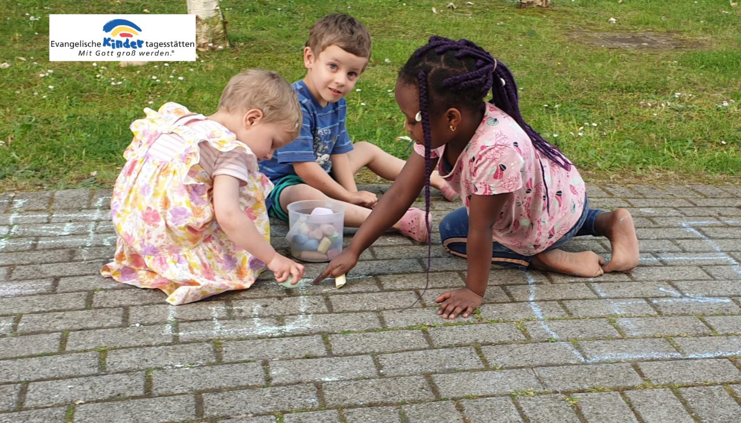 Drei Kinder sitzen auf einem gepflasterten Boden und spielen mit kleinen Gegenständen