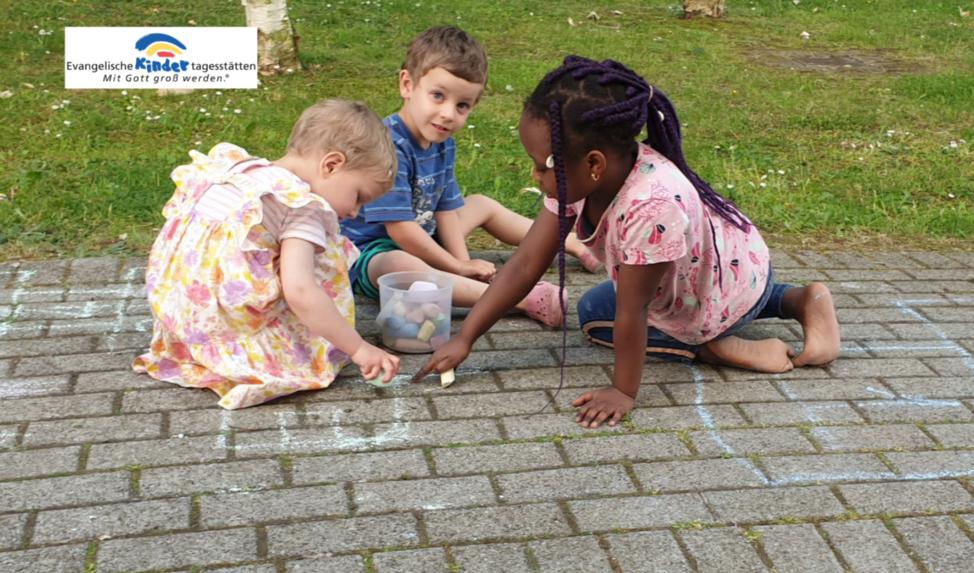 Drei Kinder sitzen auf einem gepflasterten Boden und spielen mit kleinen Gegenständen