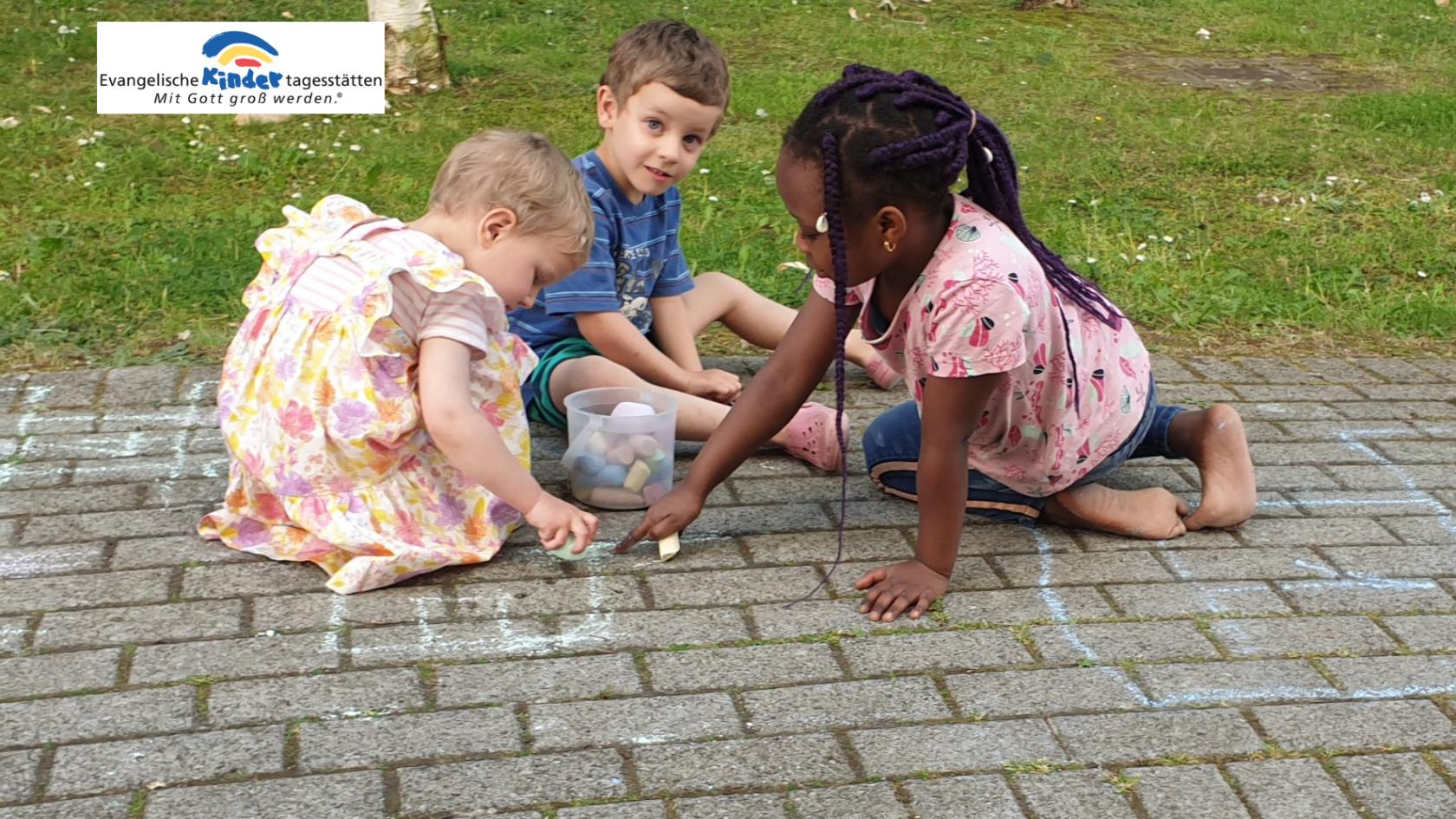Drei Kinder sitzen auf einem gepflasterten Boden und spielen mit kleinen Gegenständen