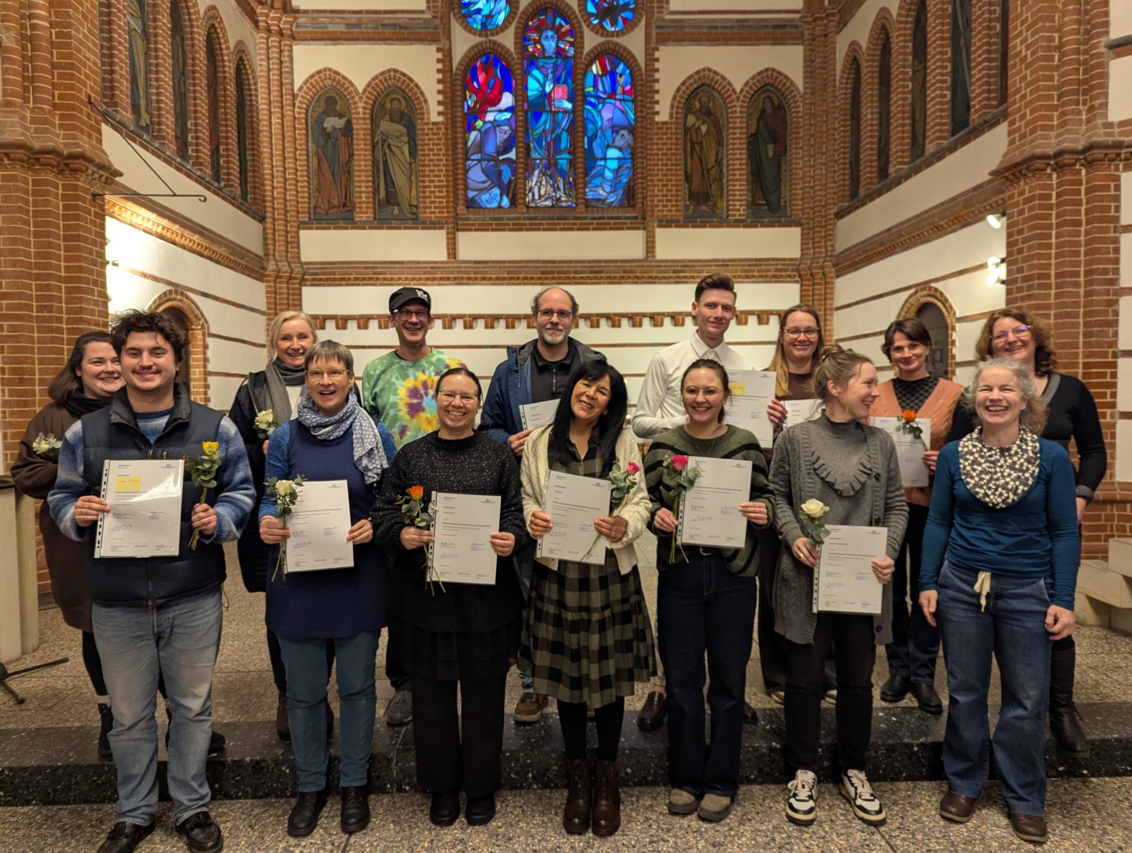 Gruppe von Menschen steht in einer Kirche und hält Zertifikate und Blumen in den Händen