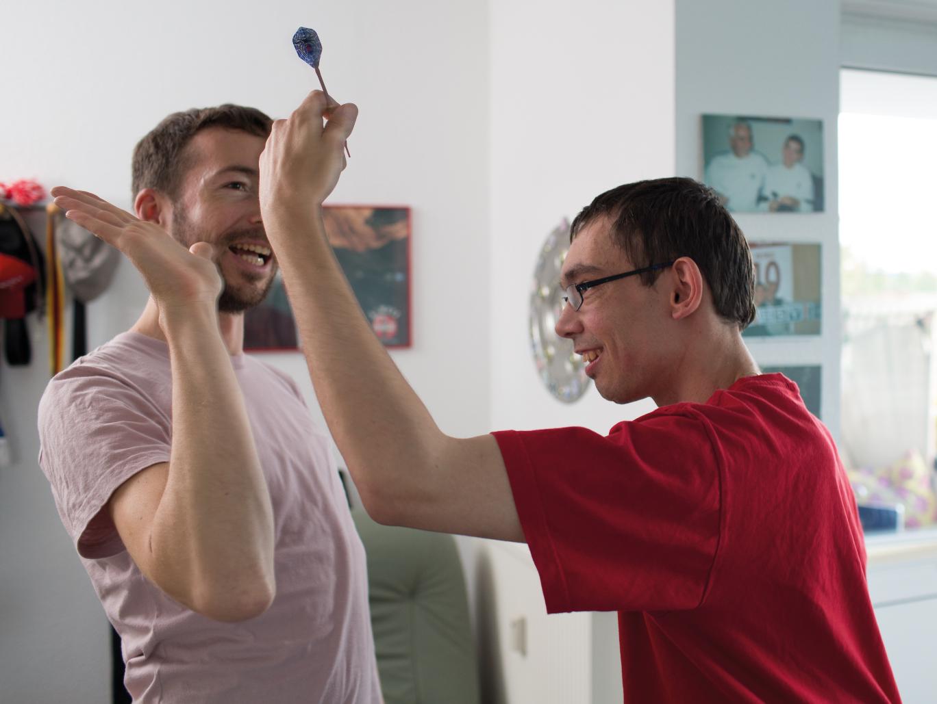 Zwei junge Männer klatschen sich ab, einer hält einen Dartpfeil in der Hand.