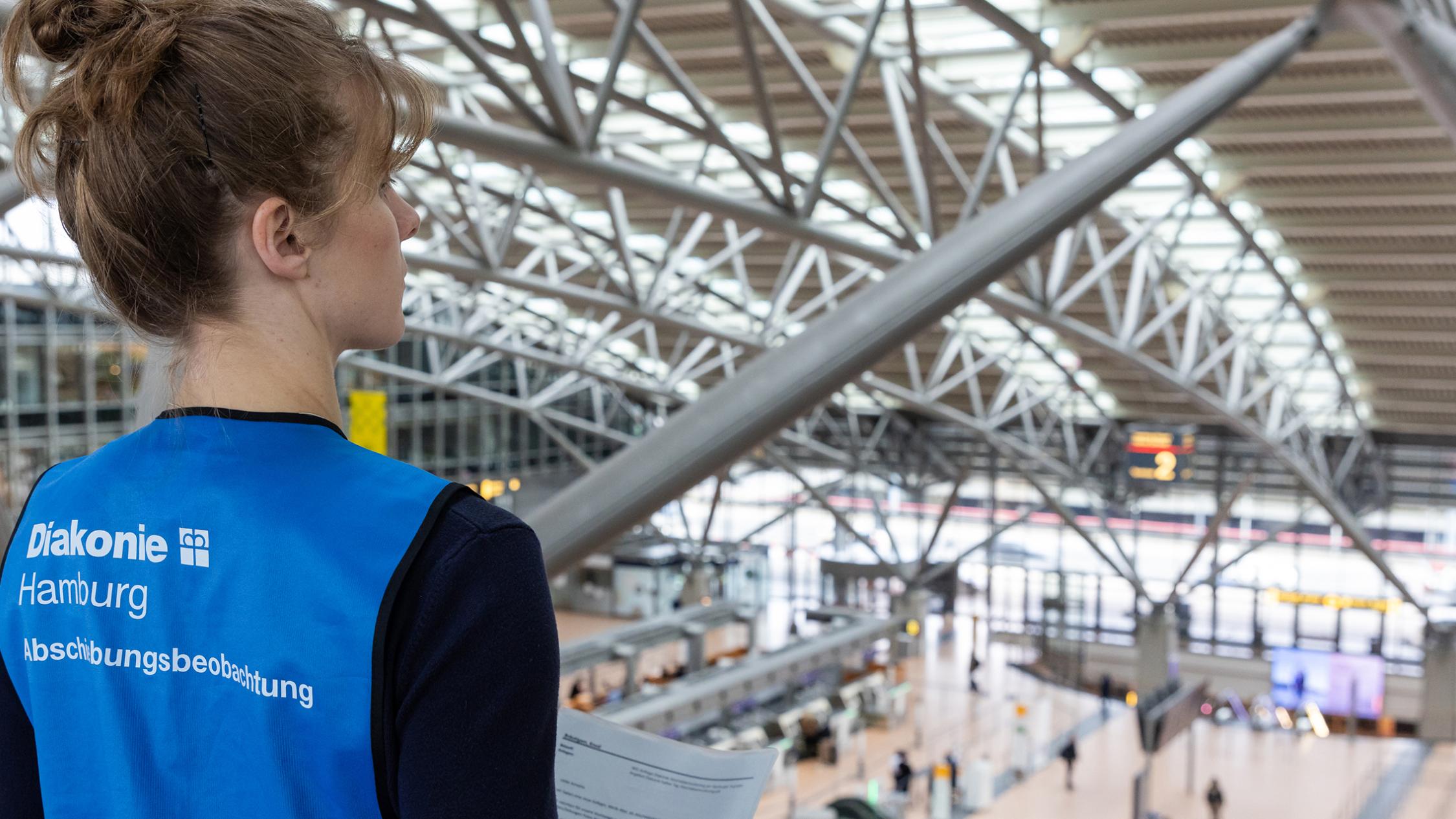 Eine Frau steht auf einer Galerie im Hamburger Flughafen und blickt auf das Geschehen in der Haupthalle hinunter.