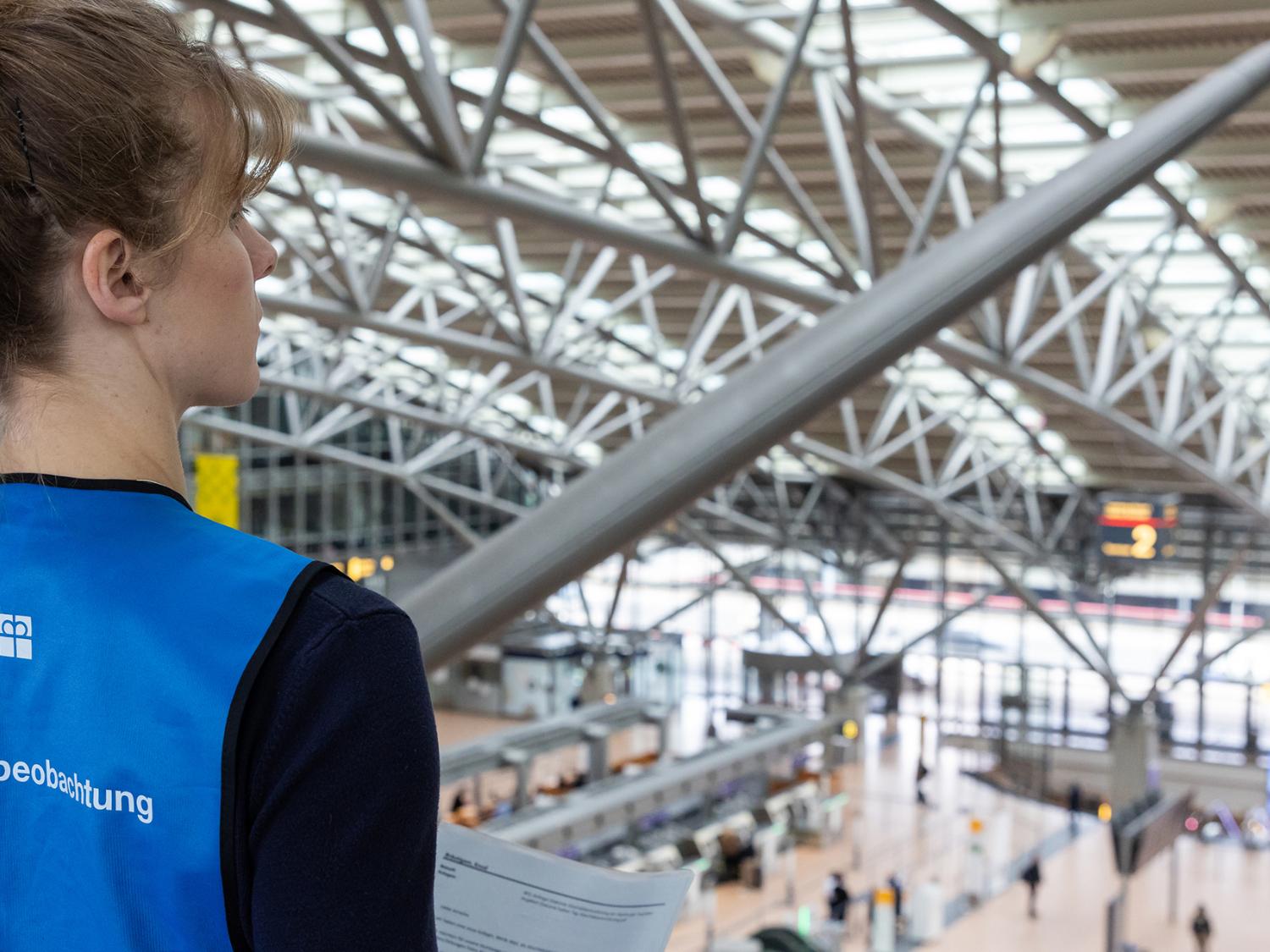 Eine Frau steht auf einer Galerie im Hamburger Flughafen und blickt auf das Geschehen in der Haupthalle hinunter.