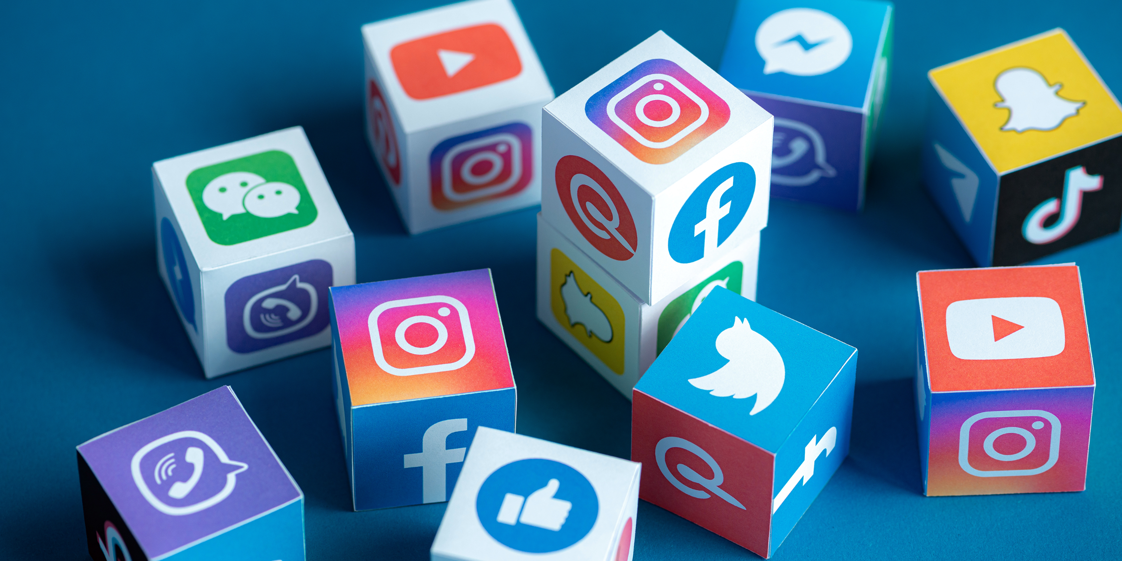 Auf einer blauen Fläche liegen viele Würfel, auf deren Seiten verschiedene Social Media-Dienste abgebildet sind.