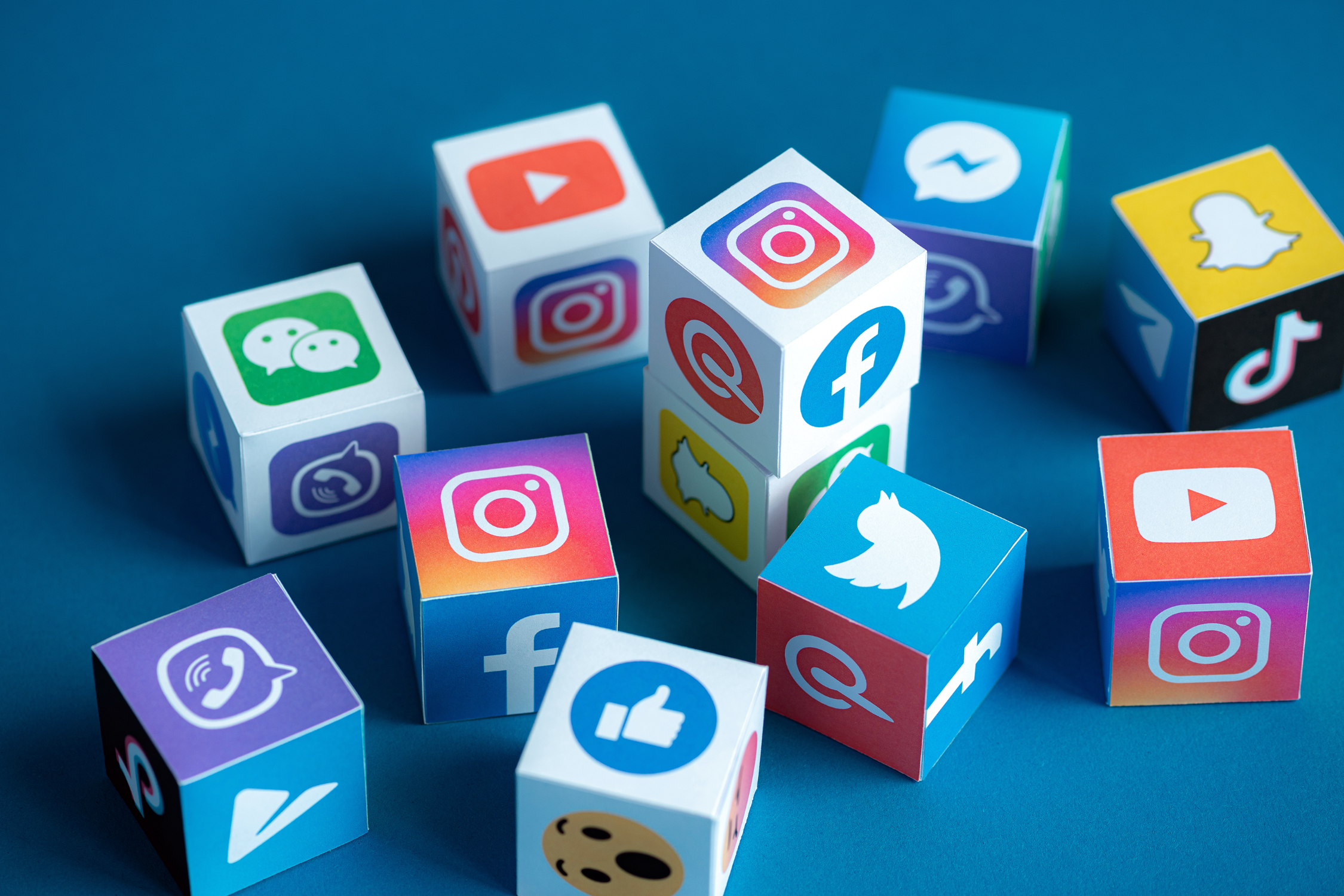 Auf einer blauen Fläche liegen viele Würfel, auf deren Seiten verschiedene Social Media-Dienste abgebildet sind.