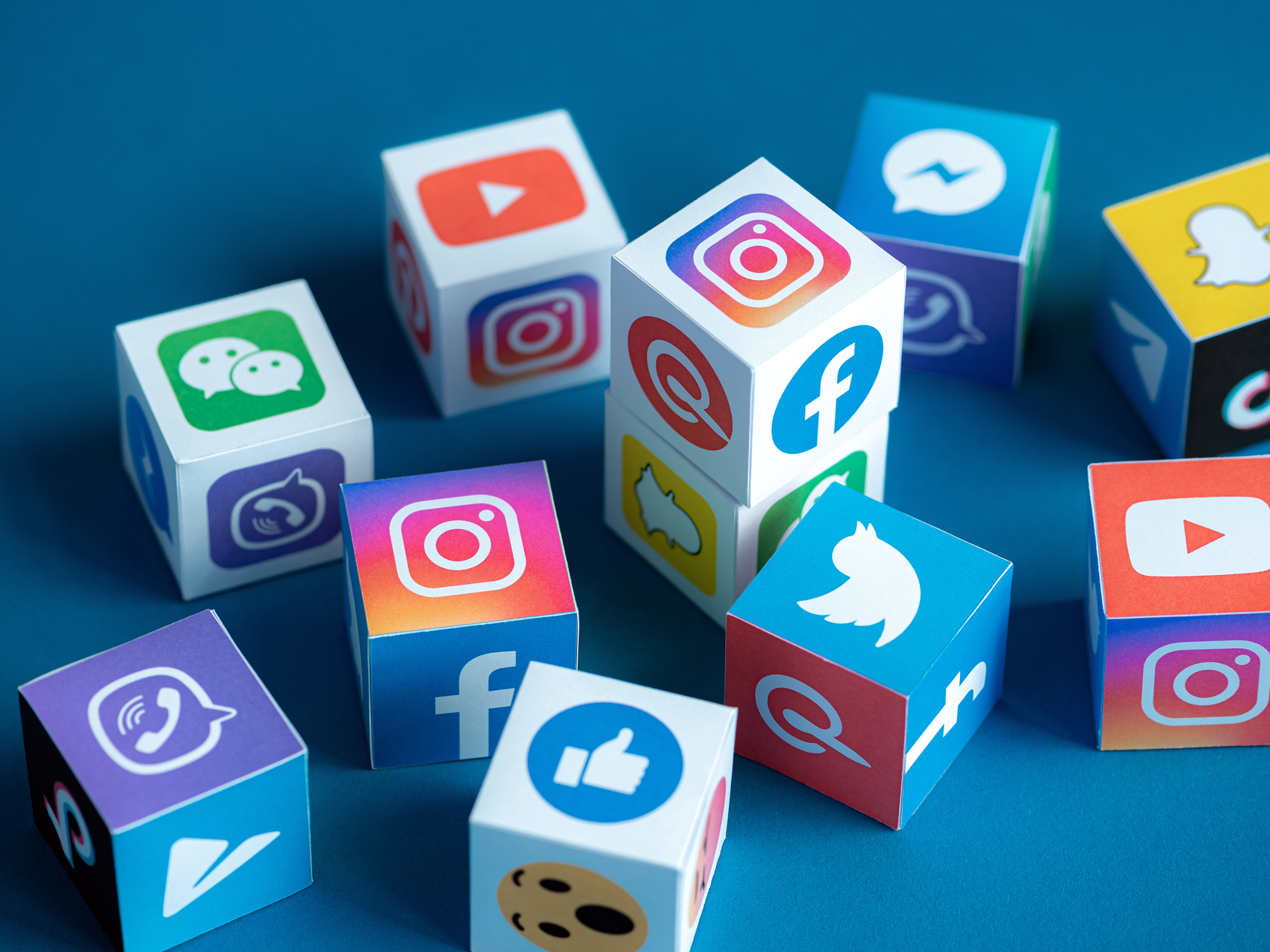 Auf einer blauen Fläche liegen viele Würfel, auf deren Seiten verschiedene Social Media-Dienste abgebildet sind.