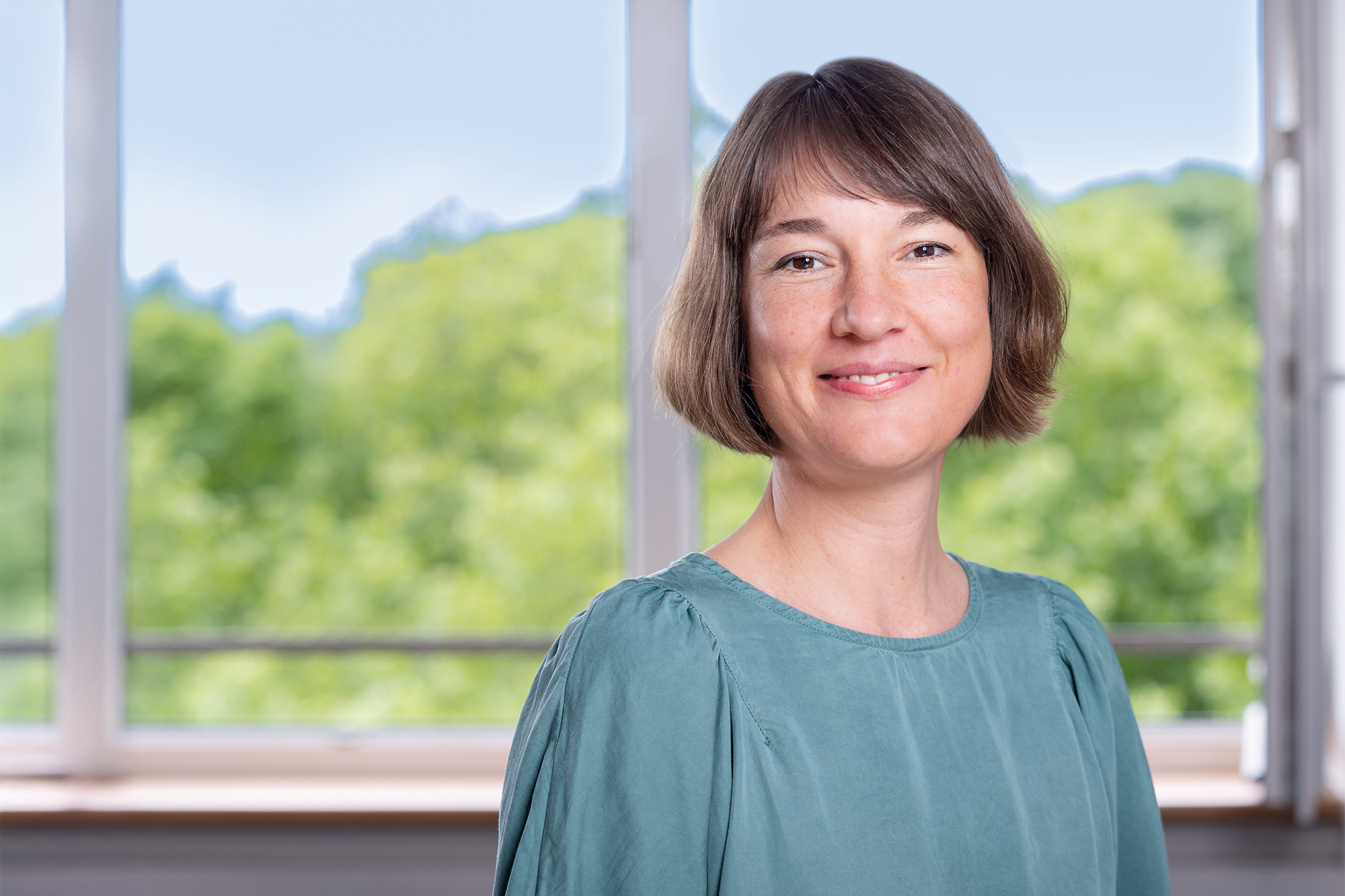 Eine Frau mit kurzen braunen Haaren lächelt in die Kamera und steht vor einem grauen Hintergrund.