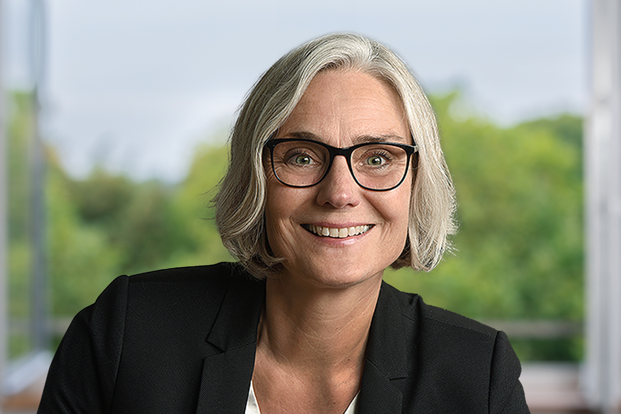 Eine Frau mit kinnlangem Haar, schwarzem Blazer und Brille lächelt in die Kamera.
