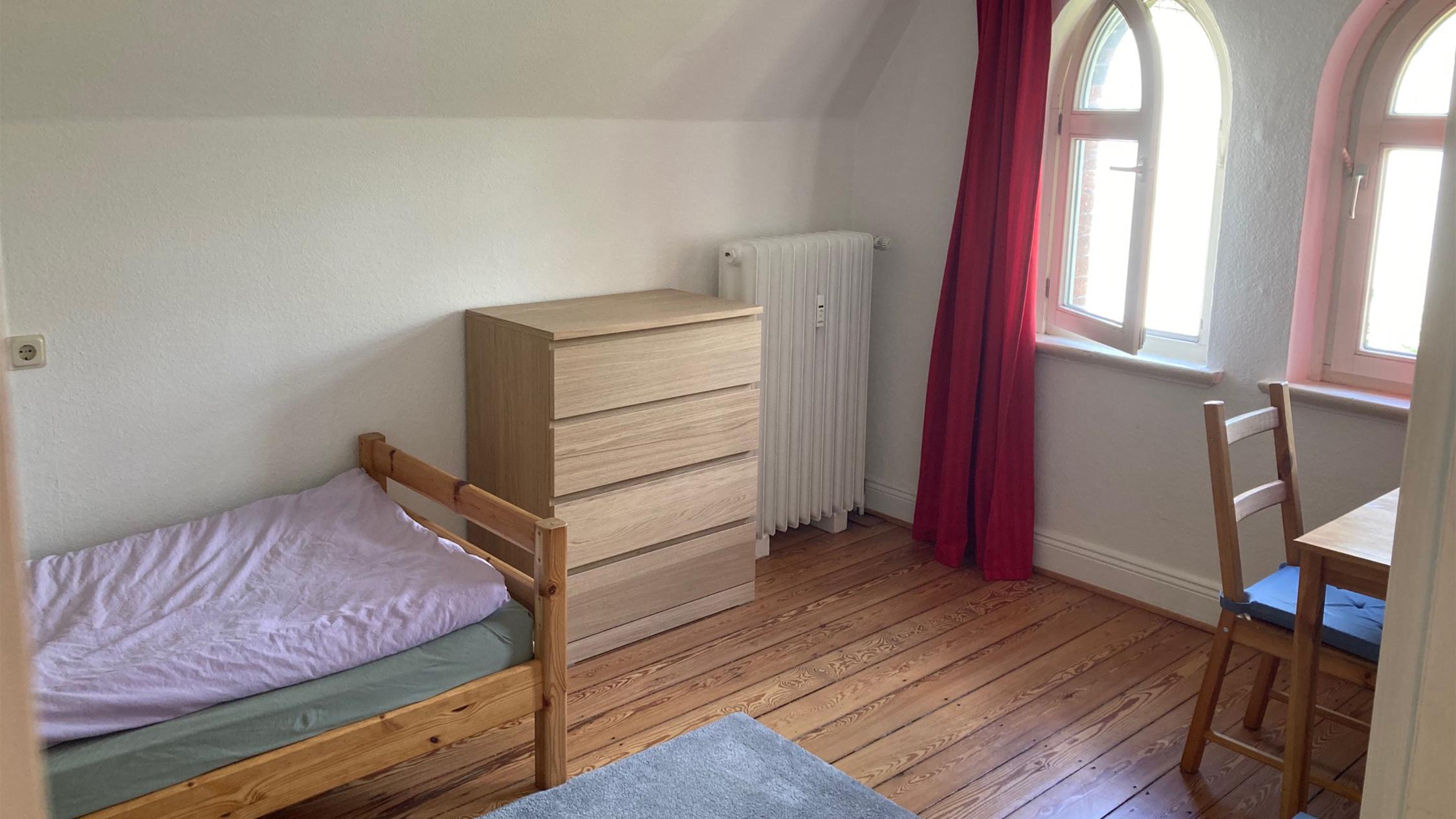 Ein Zimmer mit Bett, Kommode, Stuhl und Tisch