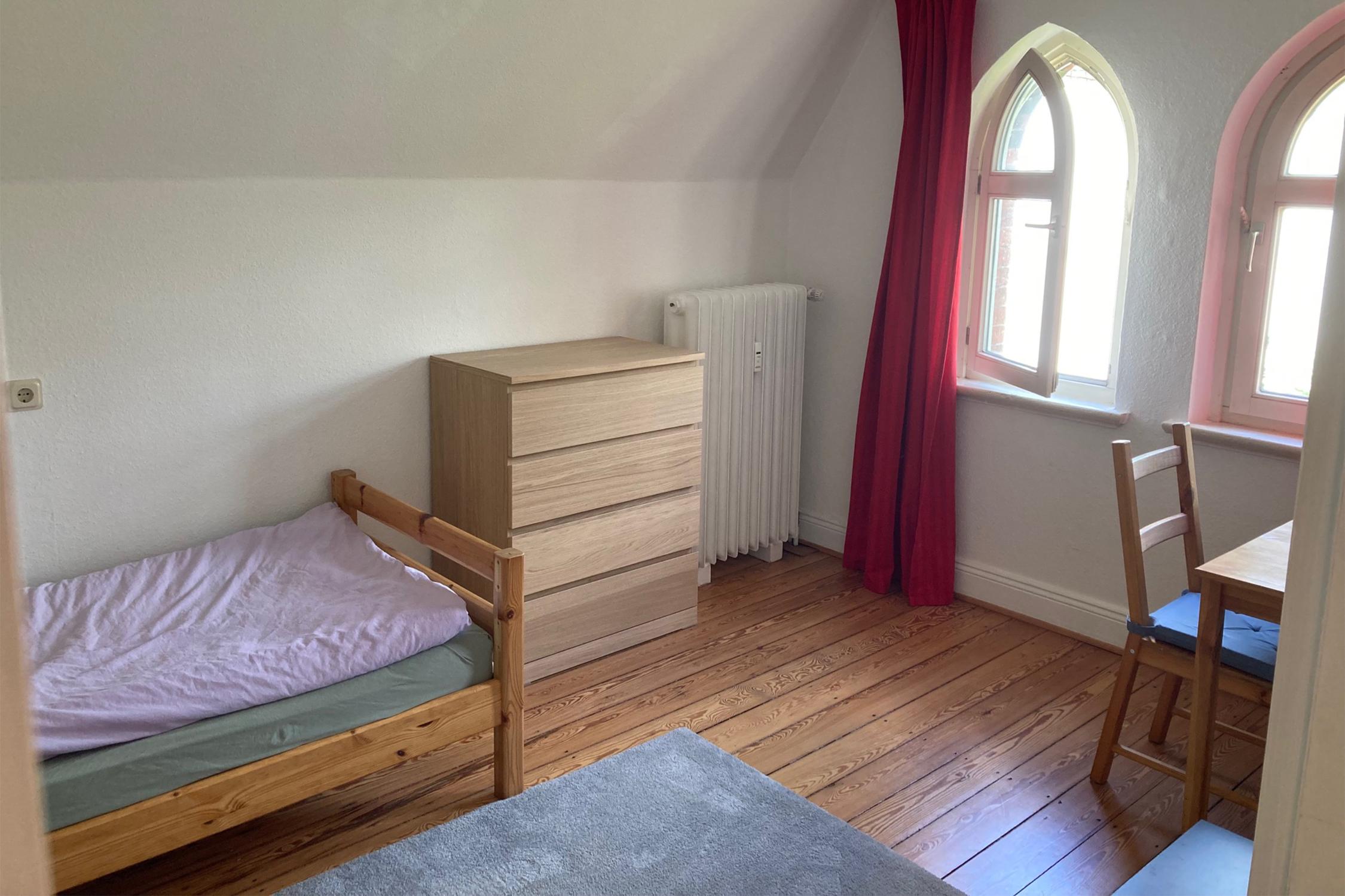 Ein Zimmer mit Bett, Kommode, Stuhl und Tisch
