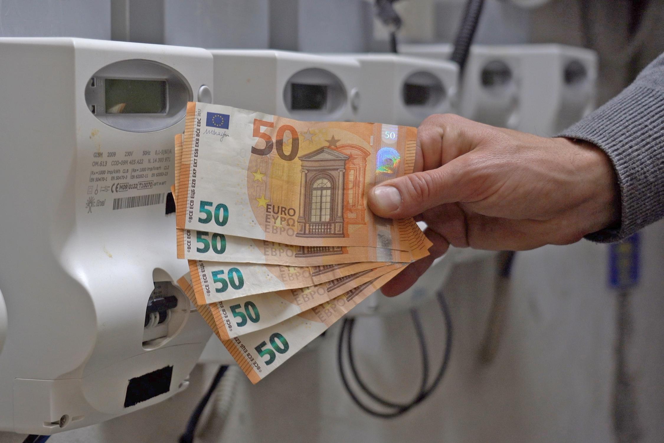 Eine Hand hält vor einen Stromverteiler fünf Fünfzig-Euro-Scheine.