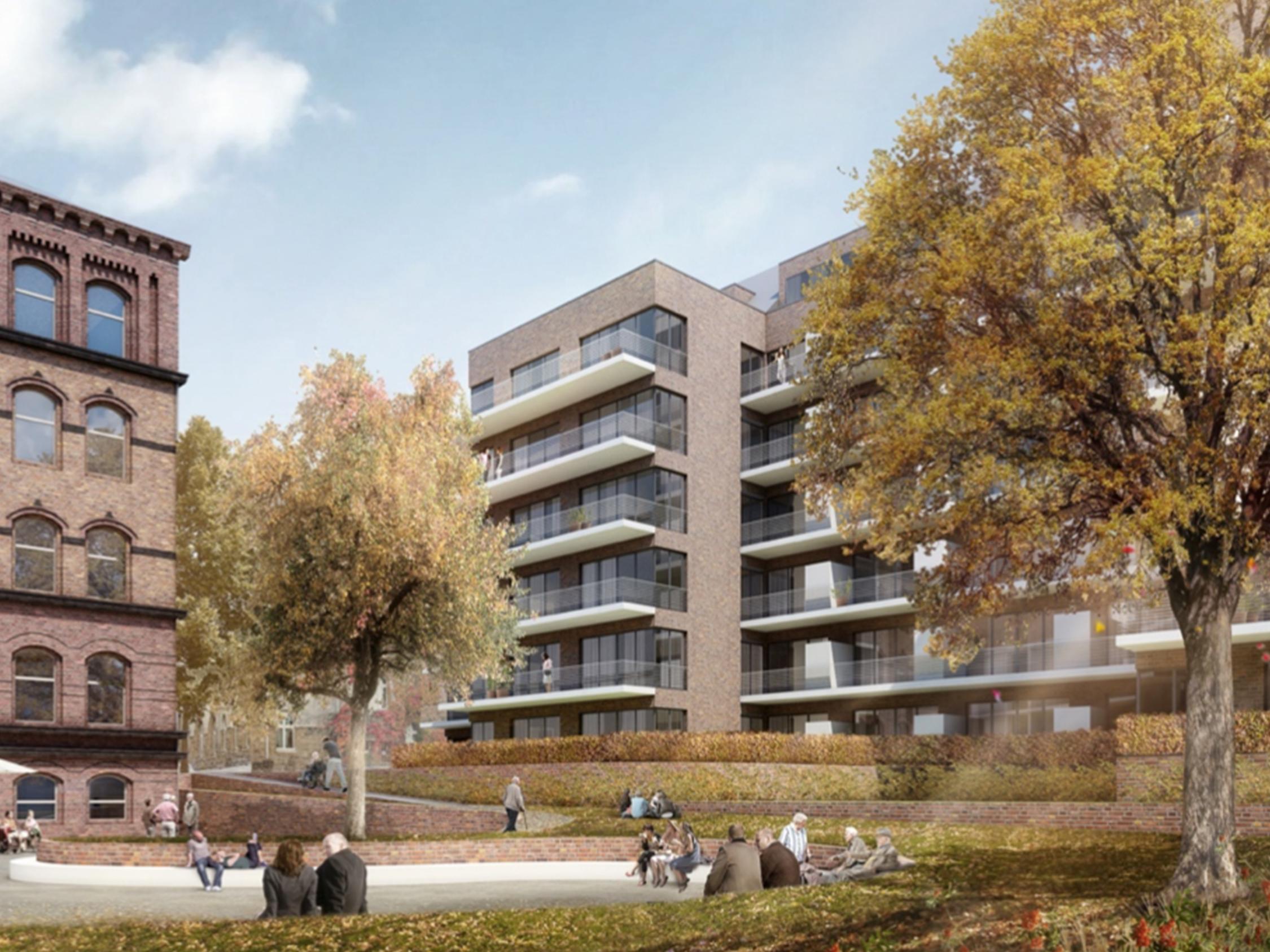 Zwischen rötlichen Gebäuden mit mehreren Wohnungen liegt ein Park, in dem sich viele Menschen aufhalten.