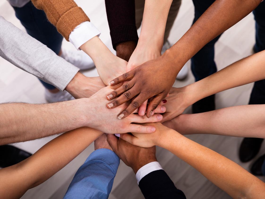Viele diverse Personen halten ihre Hände in die Mitte.