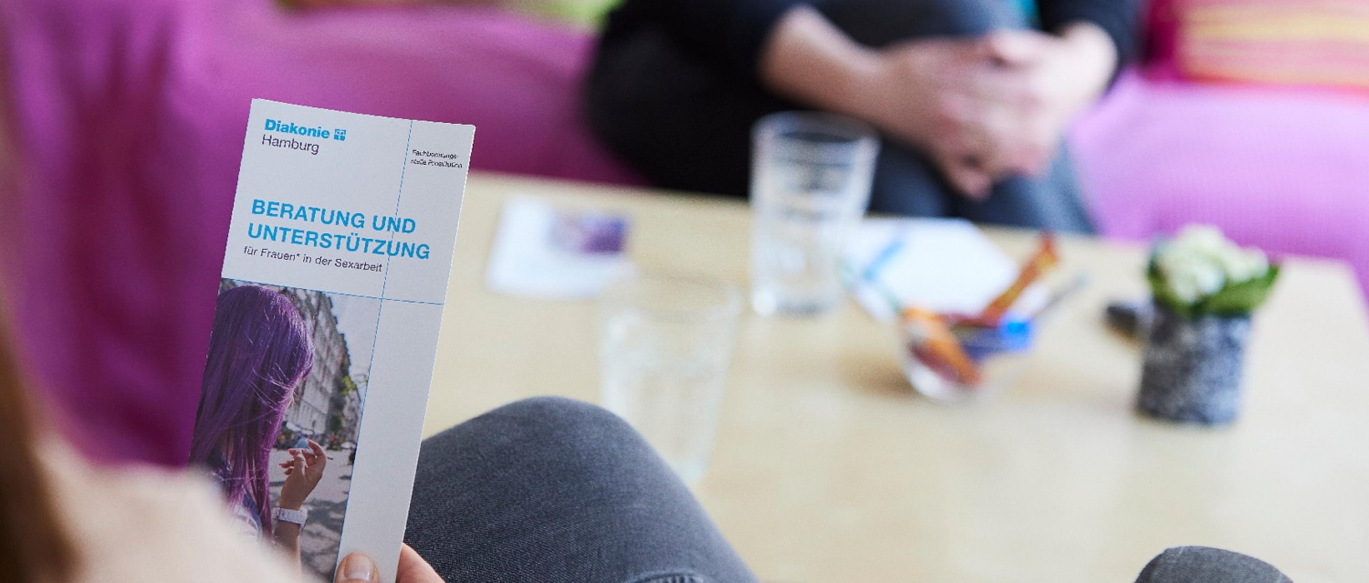 Eine Frau sitzt an einem Tisch und hält einen Beratungsflyer in der Hand.