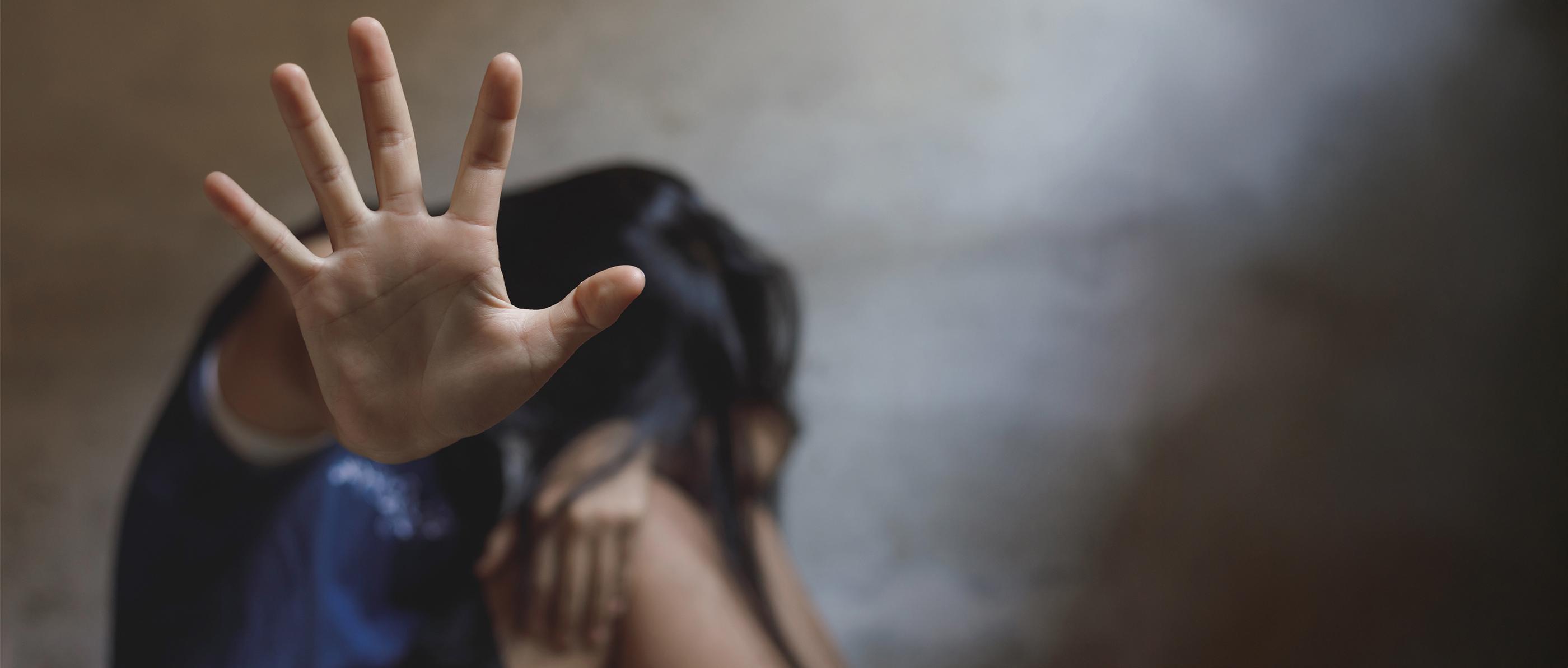 eine Frau streckt ihre Hand in die Höhe. Sie sitzt auf dem Boden und verbirgt das Gesicht zwischen den Knieen.