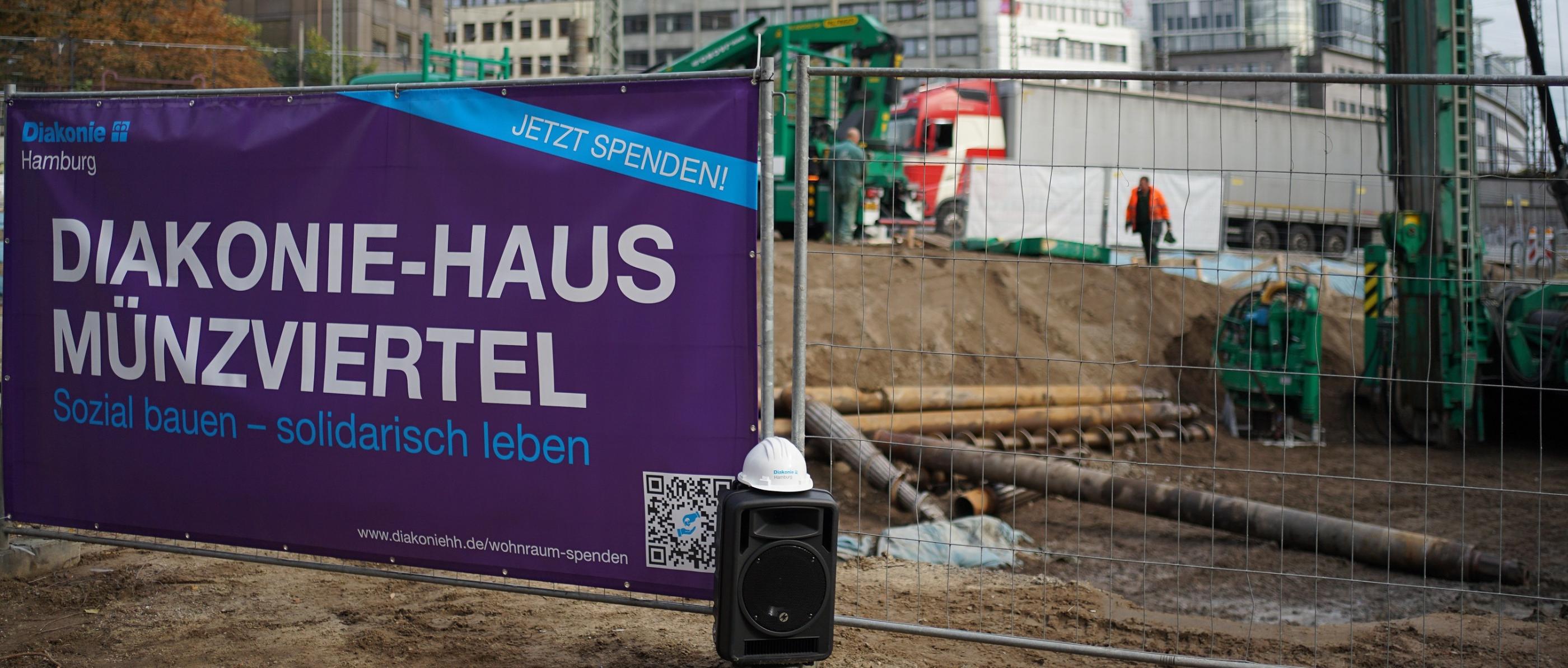 Ein Banner mit der Aufschrift Diakonie-Haus Münzviertel hängt am Bauzaun einer Baustelle.