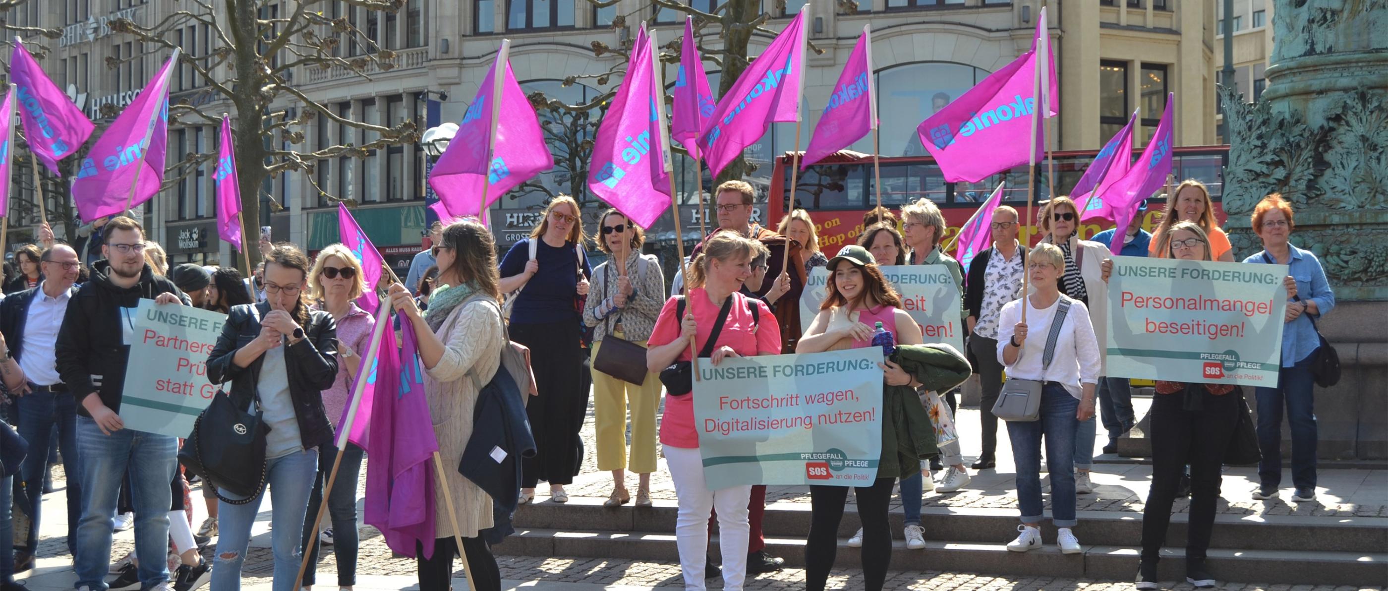 Menschen halten Diakonie-Fahnen und Transparente während einer Demonstration.