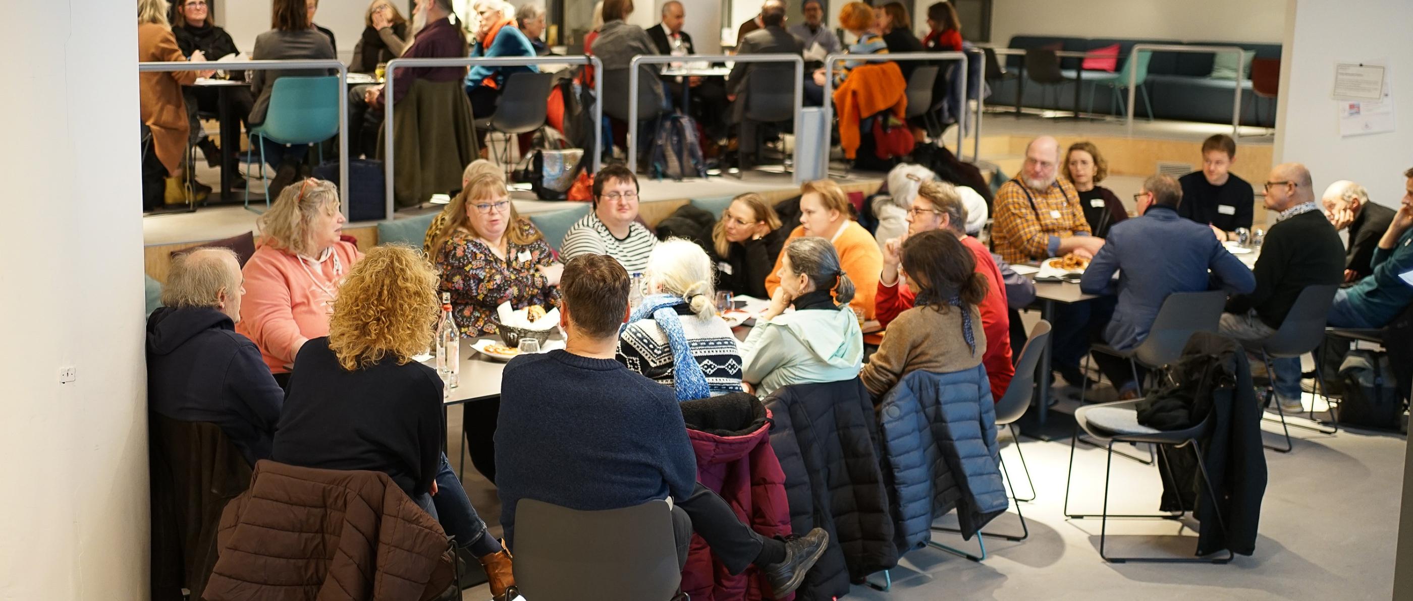 Menschen sitzen in Gruppen in einem großen Raum.