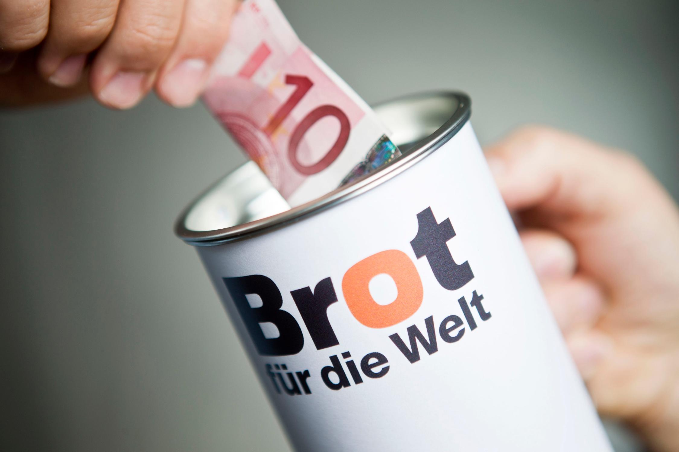 Eine Hand steckt einen Zehn-Euro-Schein in eine Spendensammeldose, auf der 'Brot für die Welt' steht.