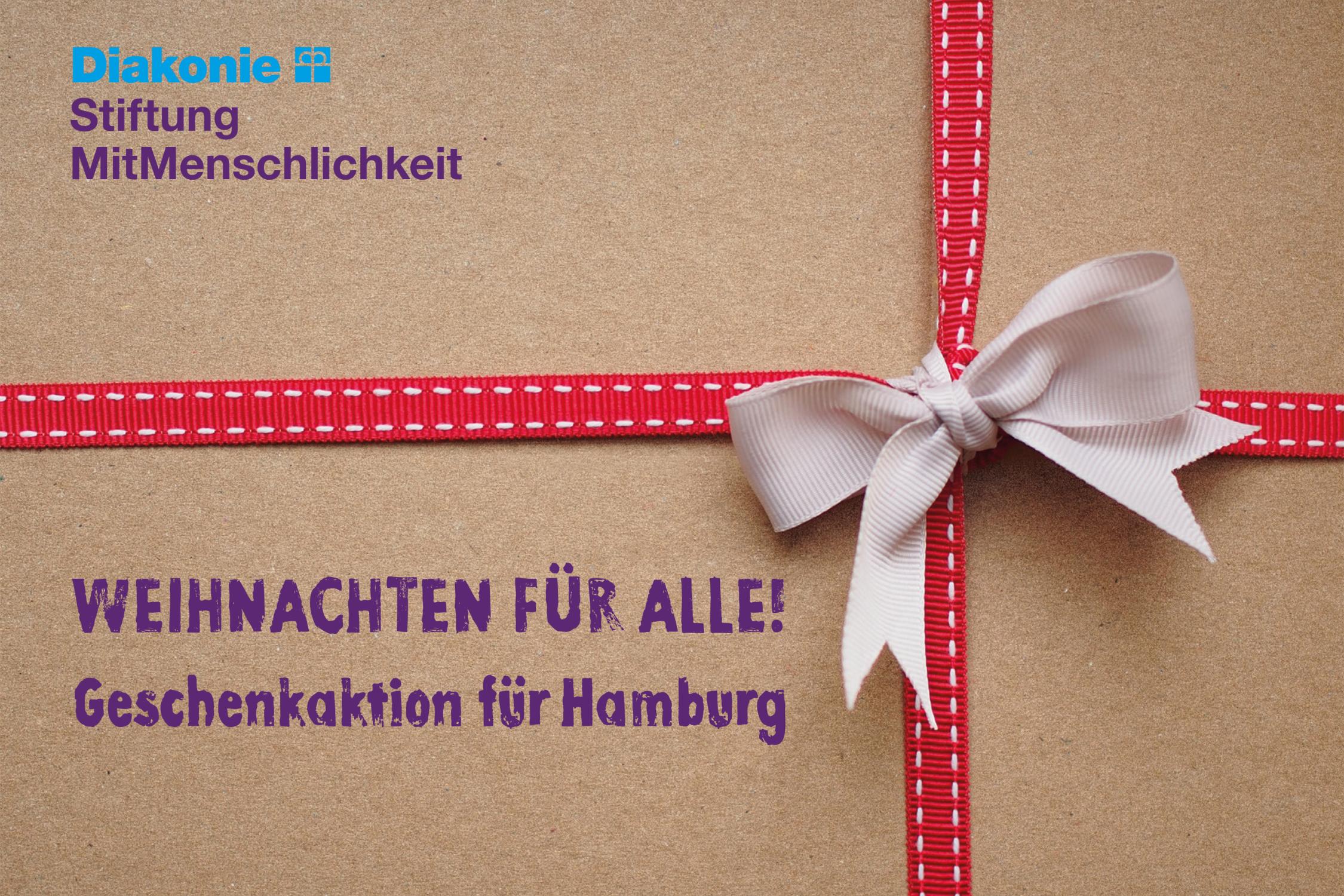 Um einen Karton ist rot-weißes Schleifenpapier geschlungen, darauf der Schriftzug 'Weihnachten für alle! Geschenkaktion für Hamburg'.