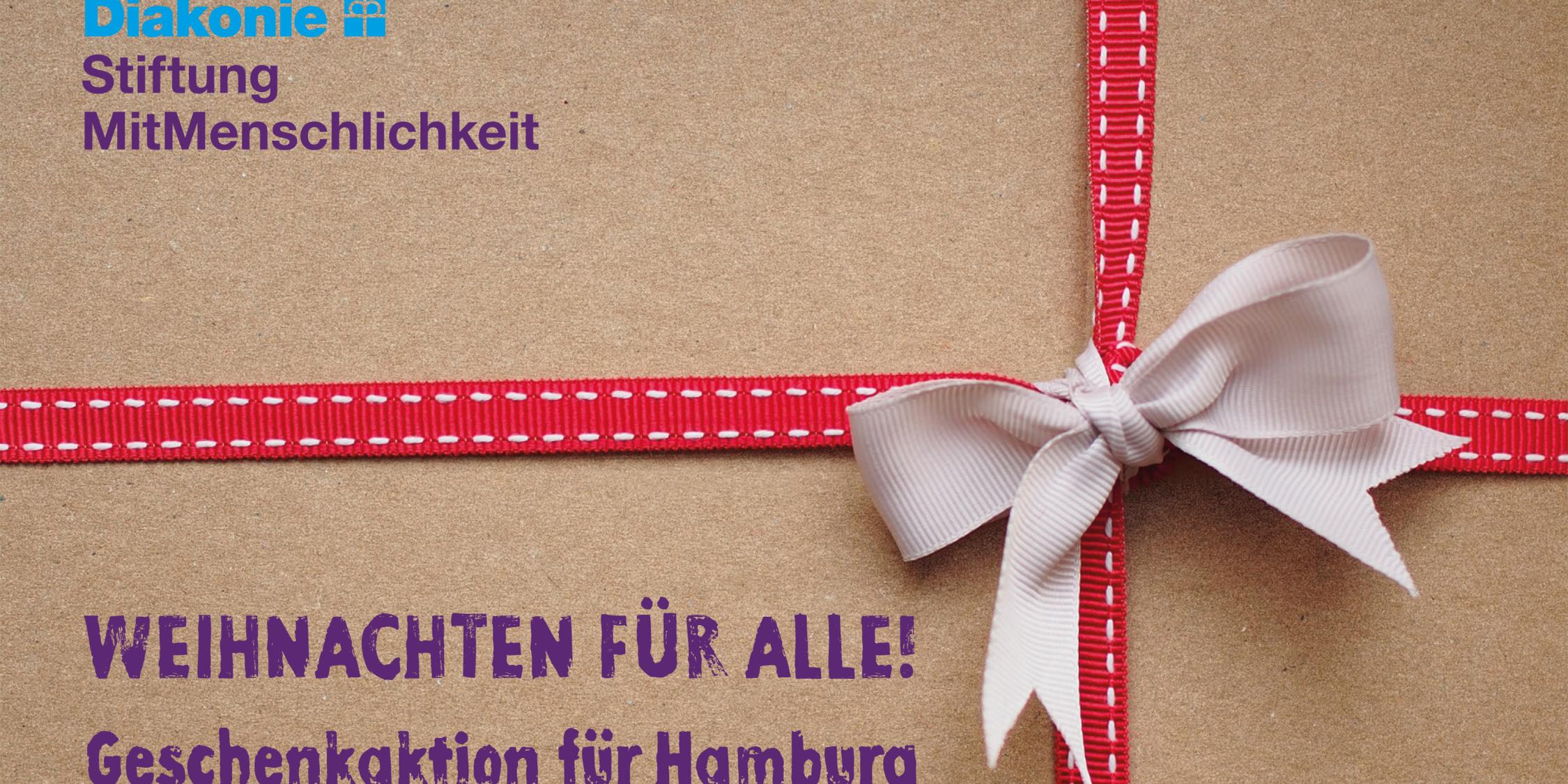 Um einen Karton ist rot-weißes Schleifenpapier geschlungen, darauf der Schriftzug 'Weihnachten für alle! Geschenkaktion für Hamburg'.