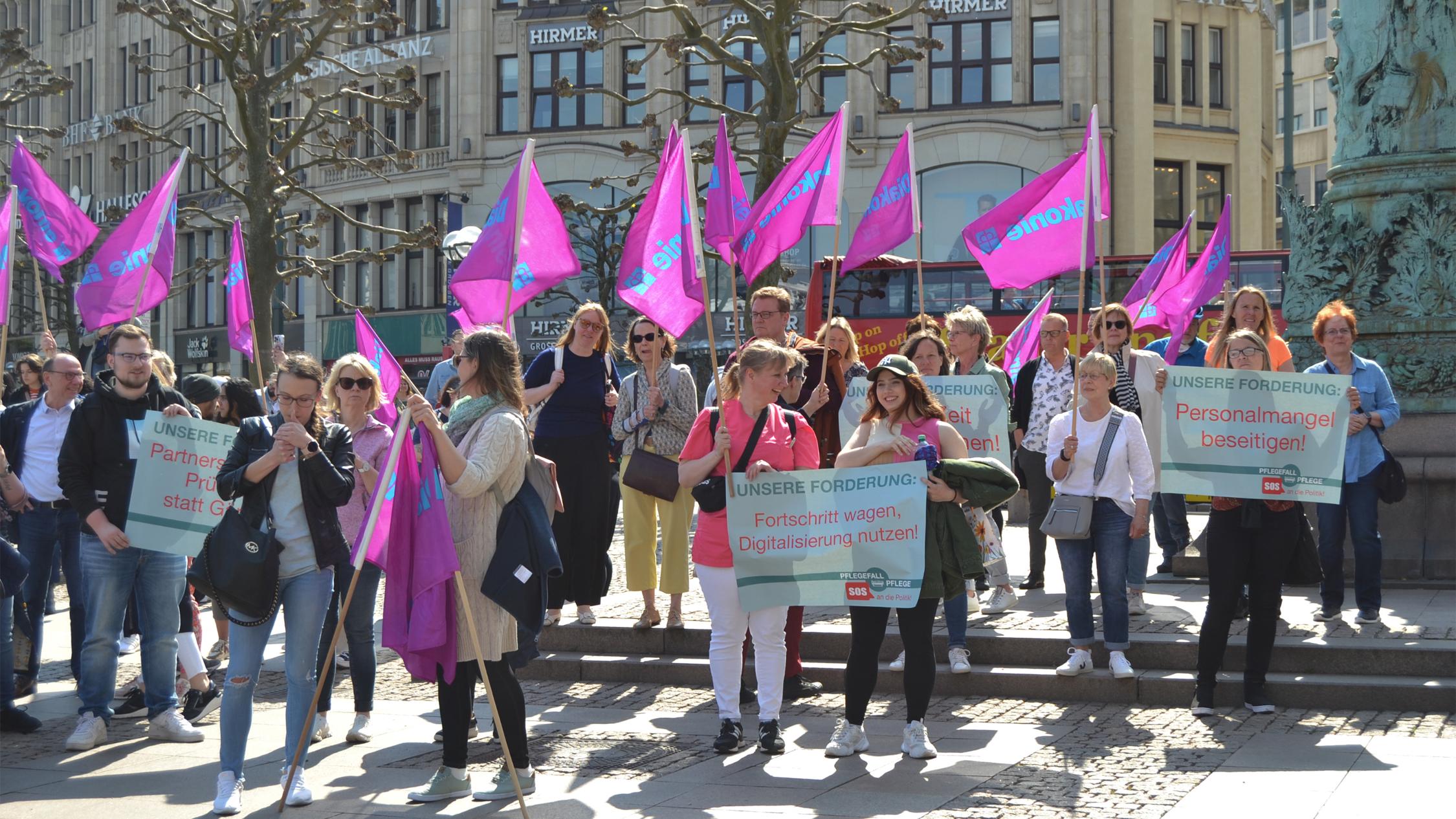 Viele Menschen laufen auf die Kamera zu, tragen Diakonie-Flaggen und halten Demo-Schilder in den Händen.