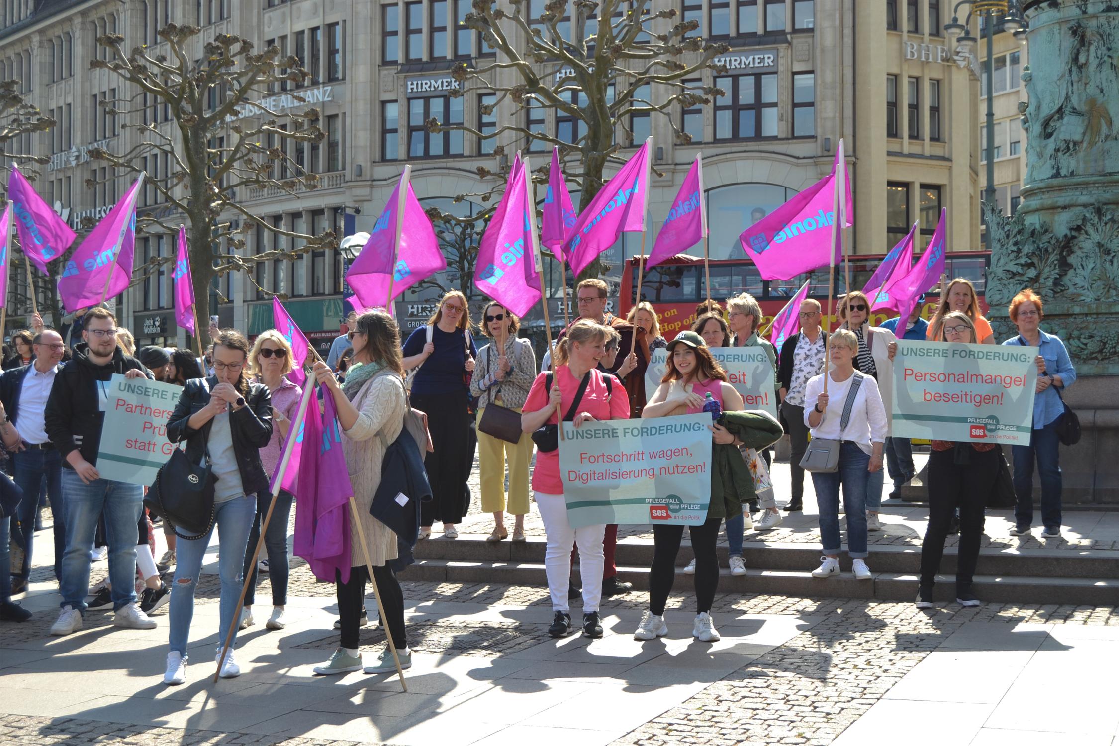 Viele Menschen laufen auf die Kamera zu, tragen Diakonie-Flaggen und halten Demo-Schilder in den Händen.