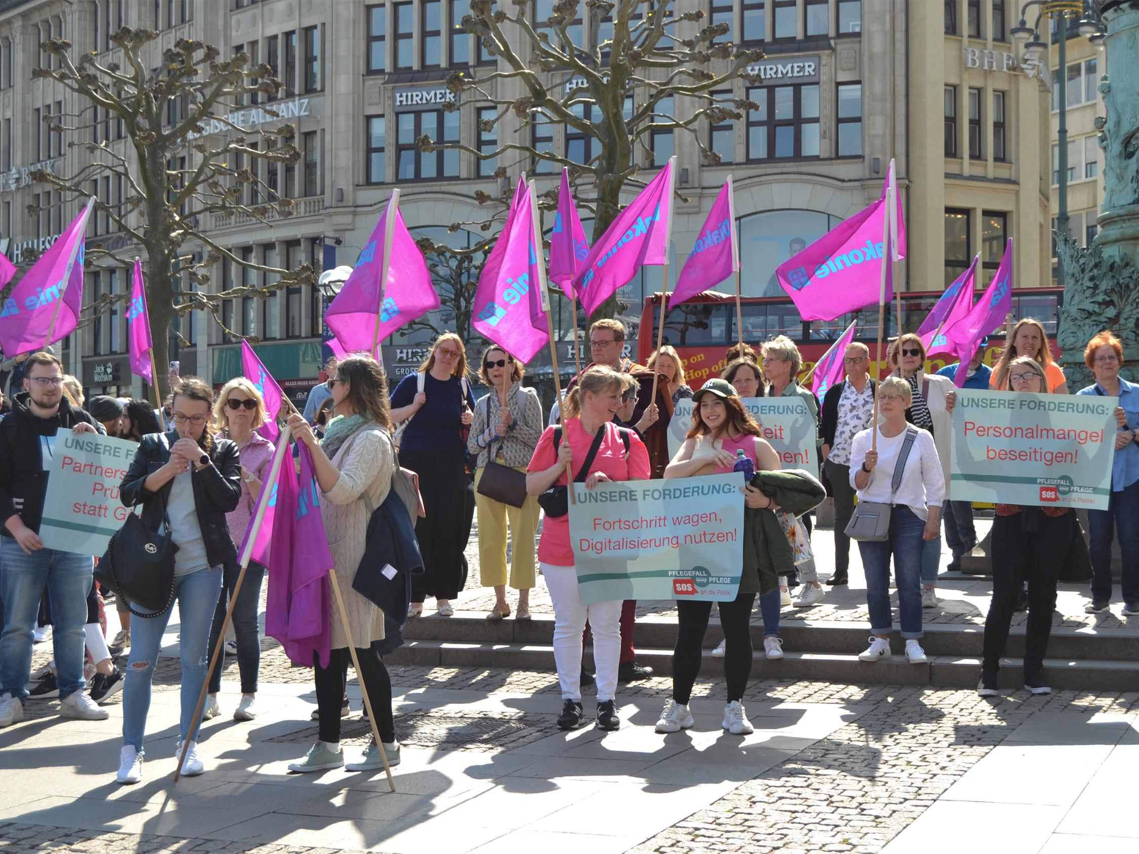Viele Menschen laufen auf die Kamera zu, tragen Diakonie-Flaggen und halten Demo-Schilder in den Händen.